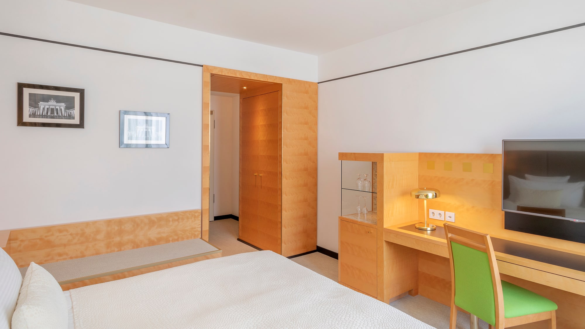 Clean hotel room with white bed, wooden desk, green chair, and TV.