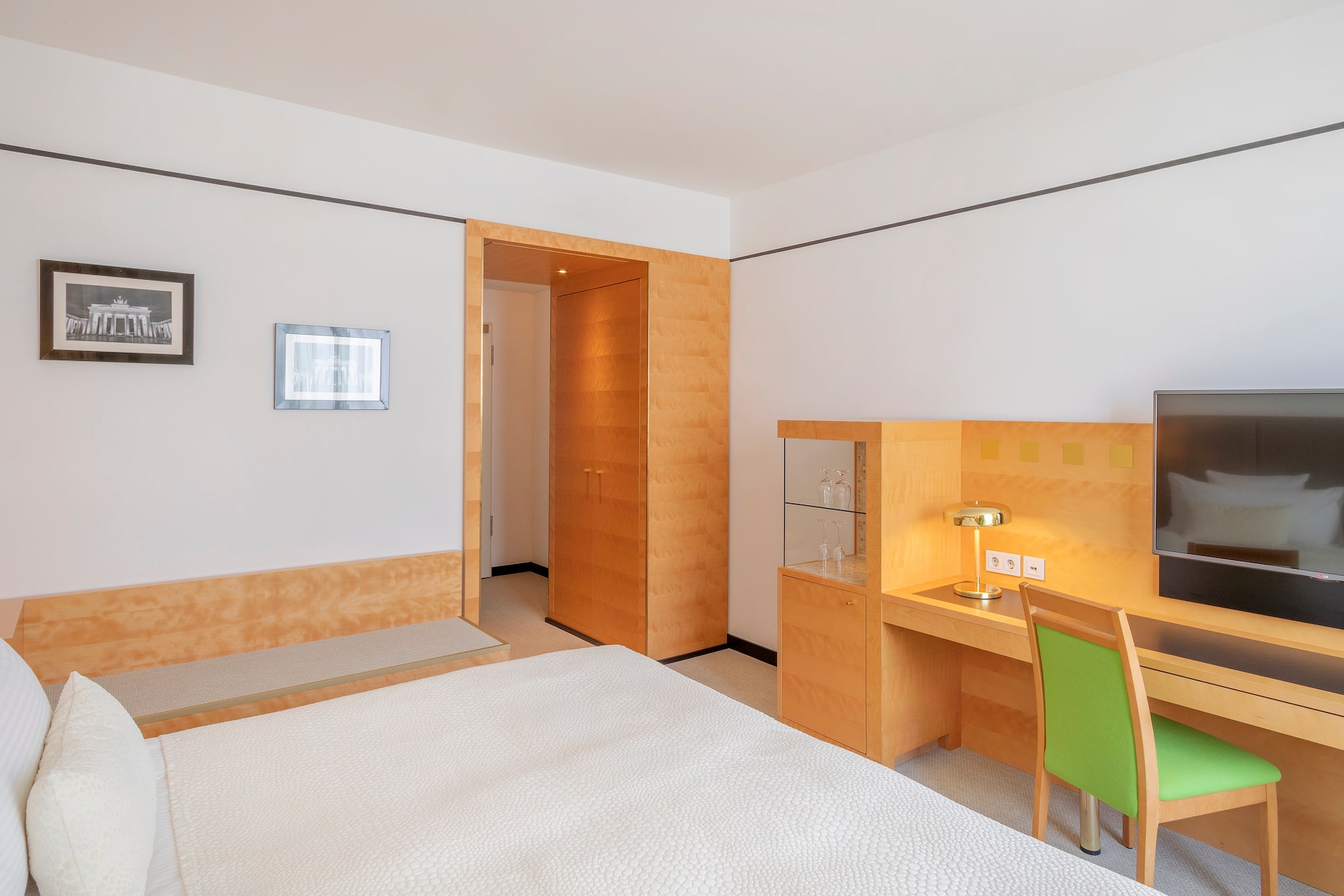 Clean hotel room with white bed, wooden desk, green chair, and TV.