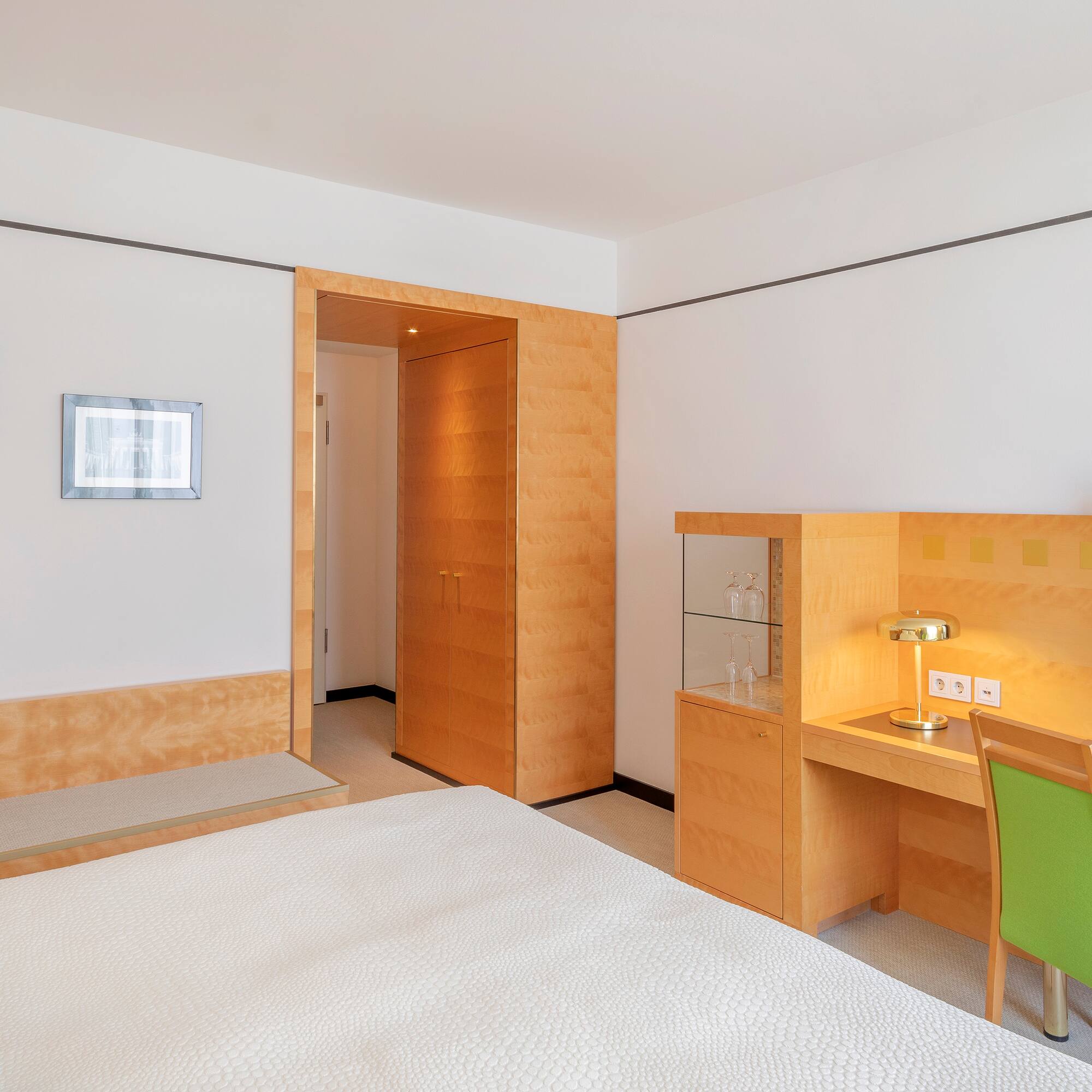 Clean hotel room with white bed, wooden desk, green chair, and TV.