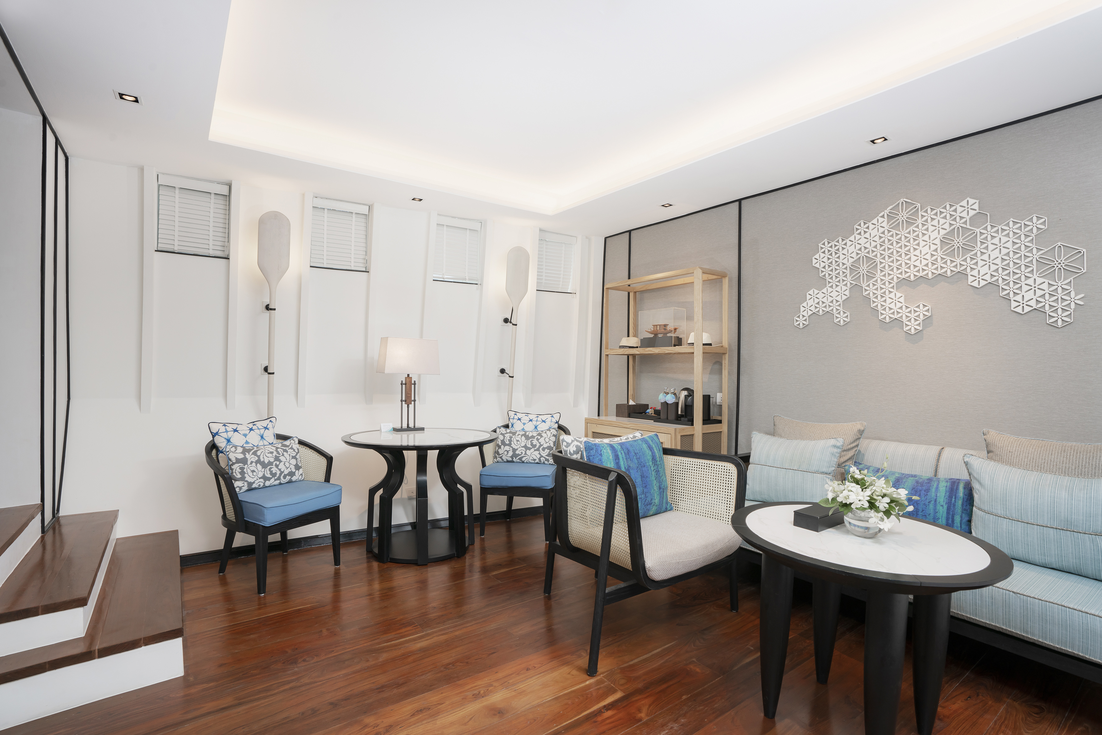 Modern lounge with blue seating, dark hardwood floor, geometric wall art.