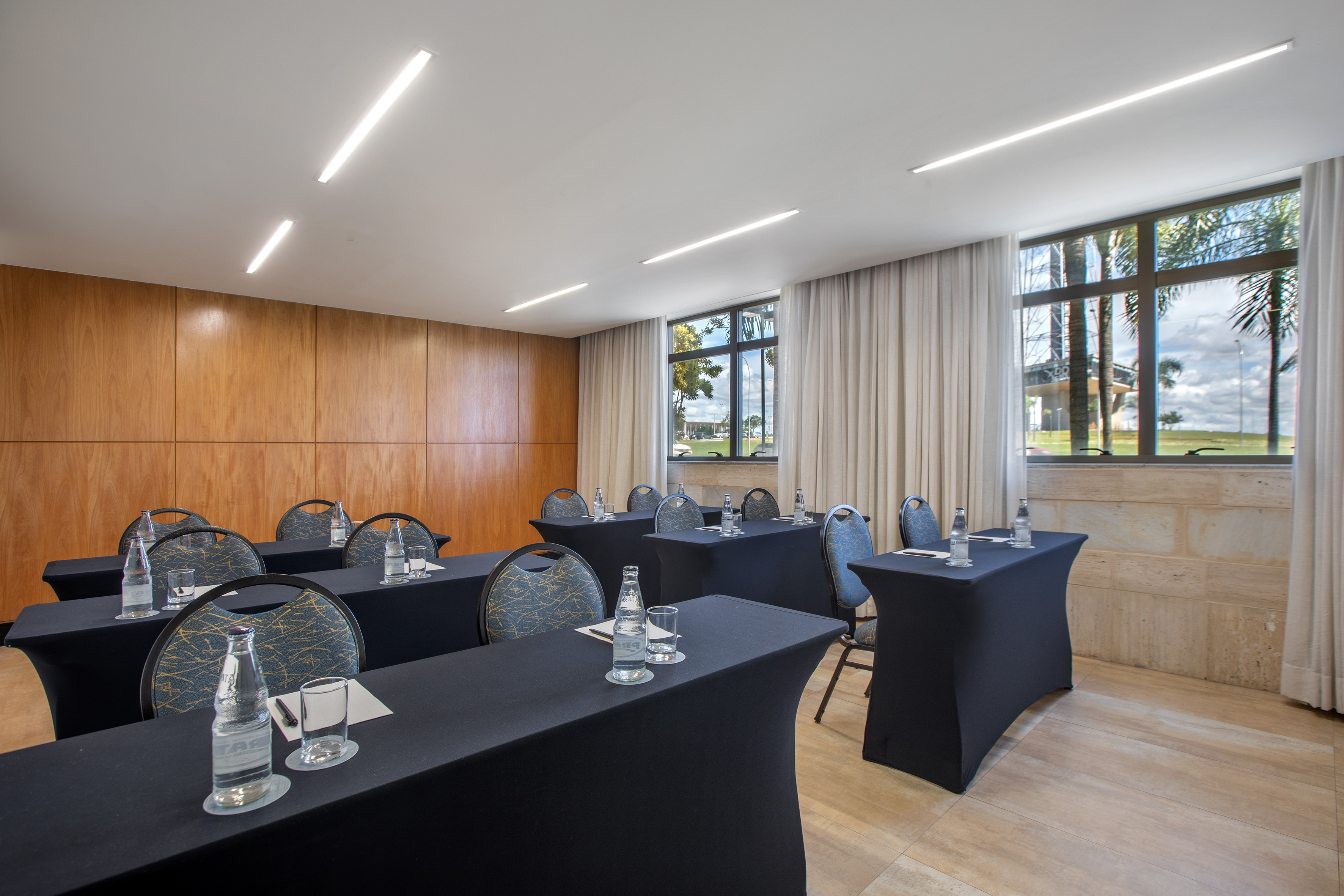 Modern hotel meeting room with black tables, chairs, wood walls, and bright windows.