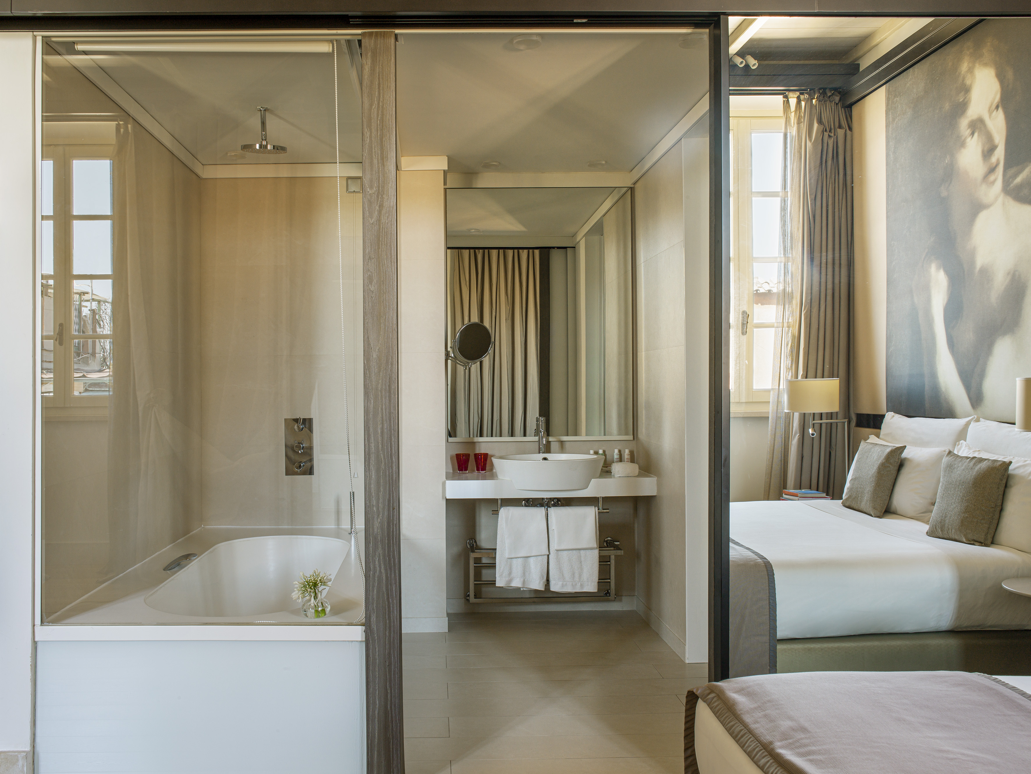 Luxury hotel suite with glass bathroom, tub, shower, vanity, and bed.
