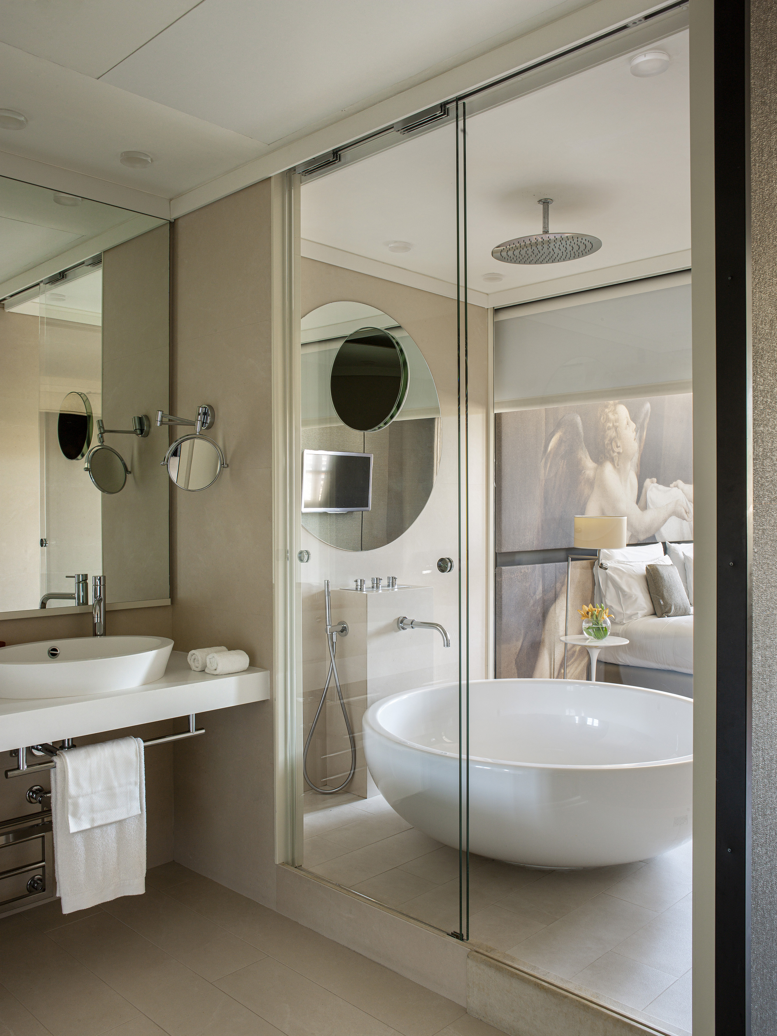 Modern bathroom with freestanding tub, glass shower, and adjoining bedroom.