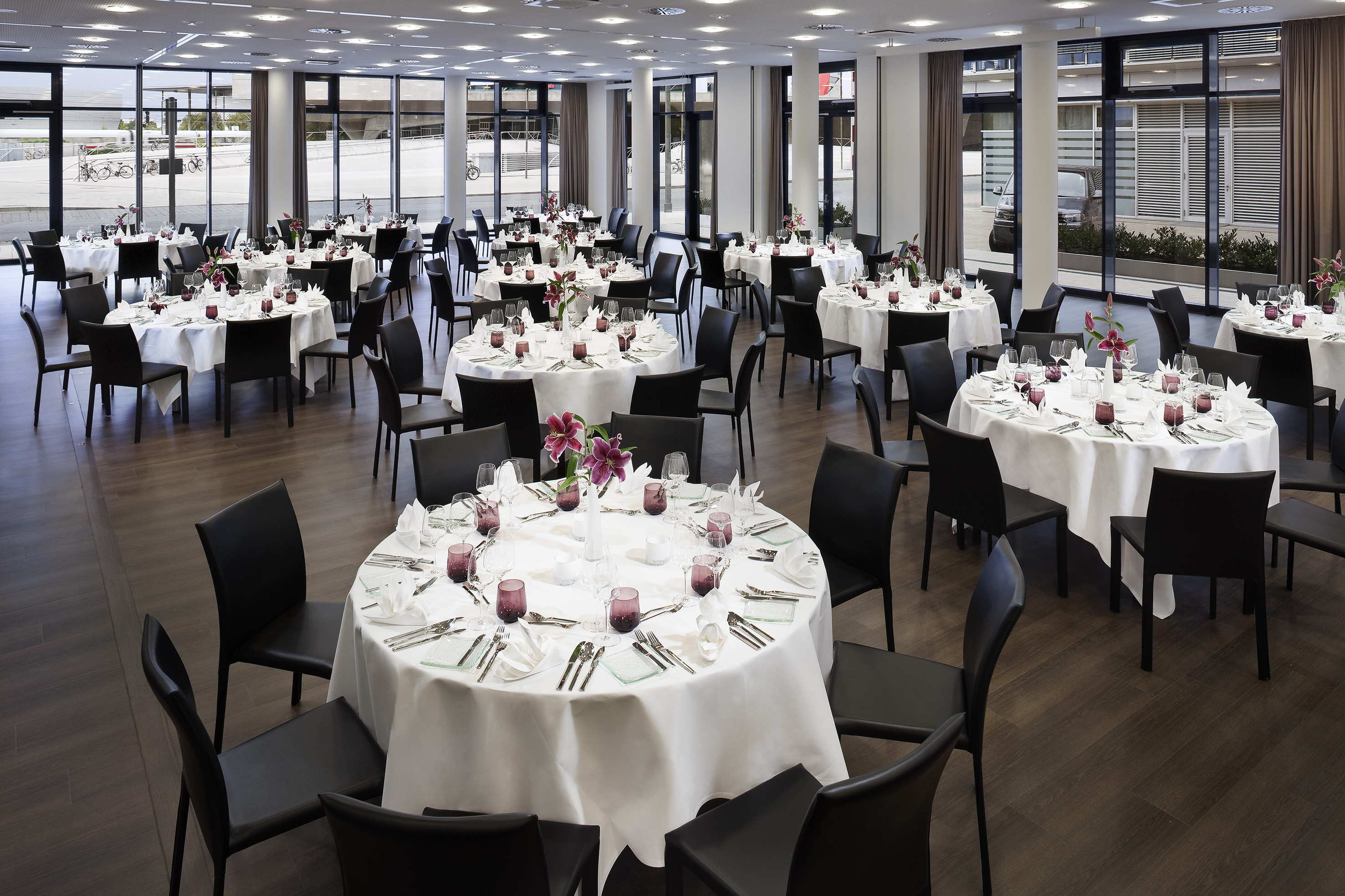 Banquet hall with round tables, white linens, black chairs, event setup. - Volkswagen - INNSiDE Wolfsburg, Wolfsburg