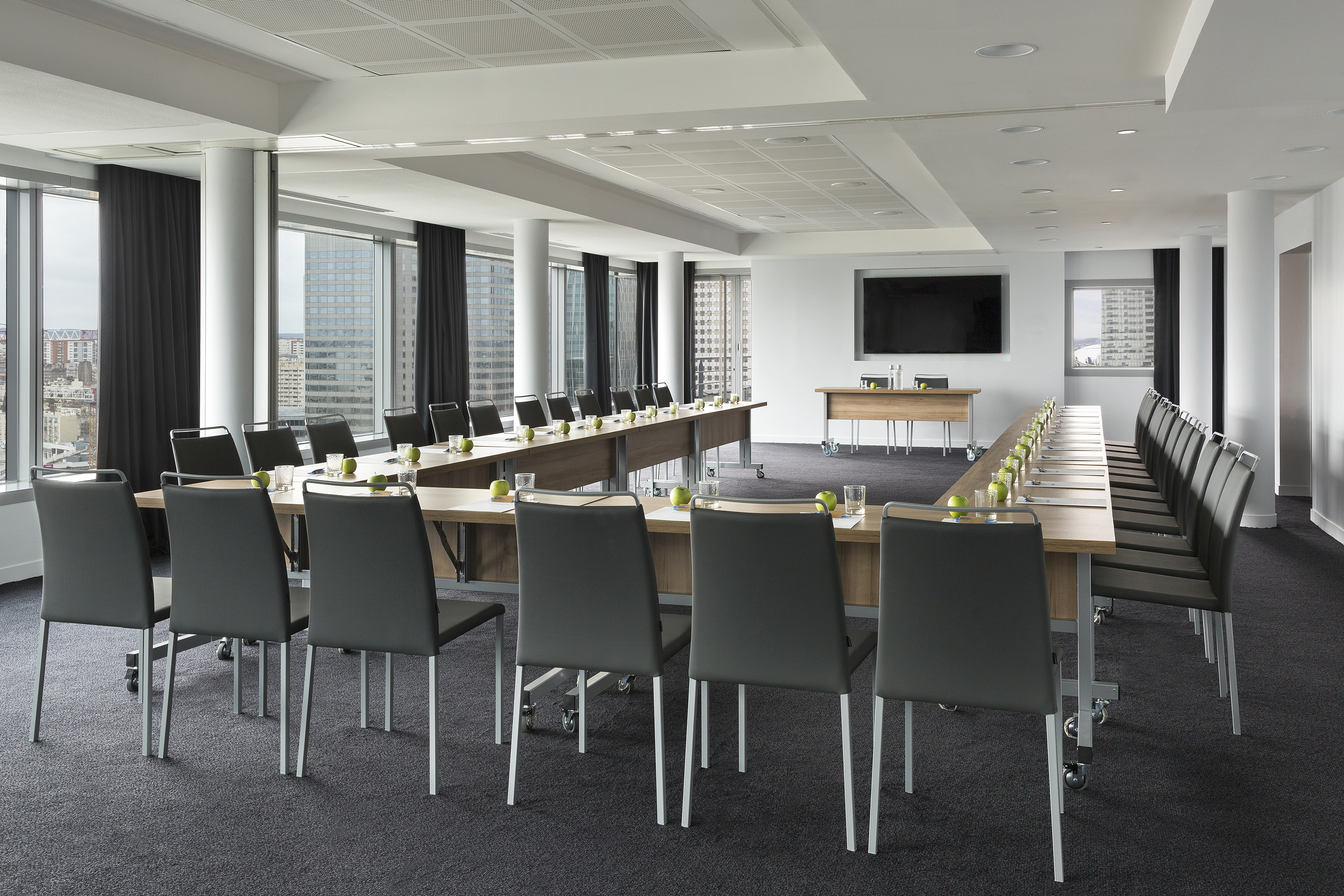 Modern U-shaped conference room with city view windows and presentation screen.