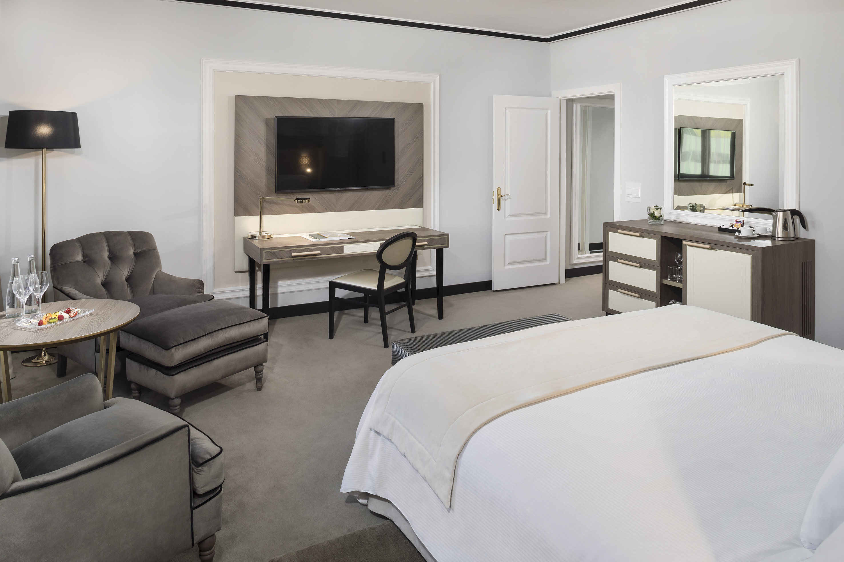 Elegant hotel suite with King bed, desk, armchairs, and refreshment station.