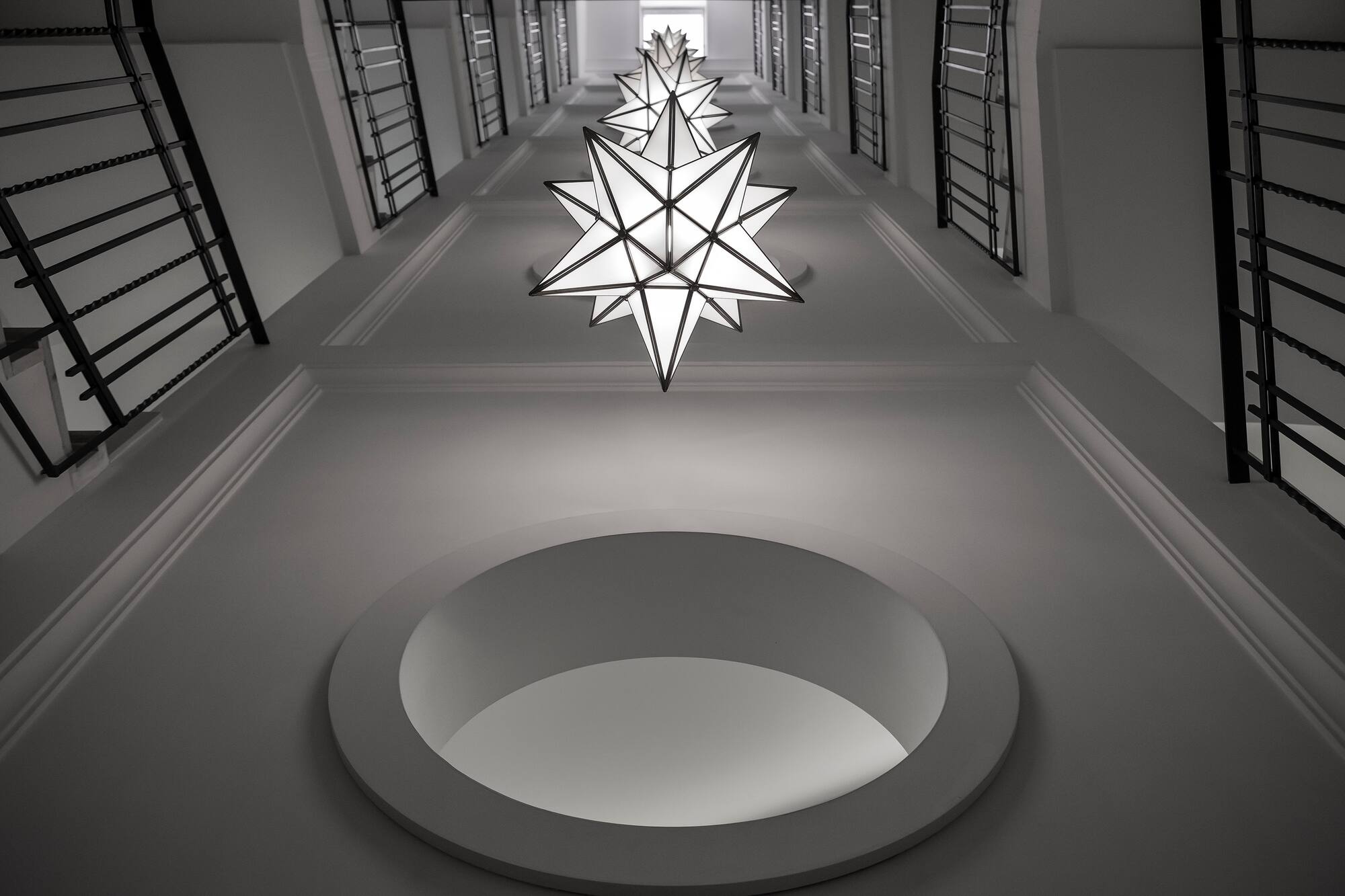 Modern white stairwell, star-shaped lights, black railings, circular ceiling.