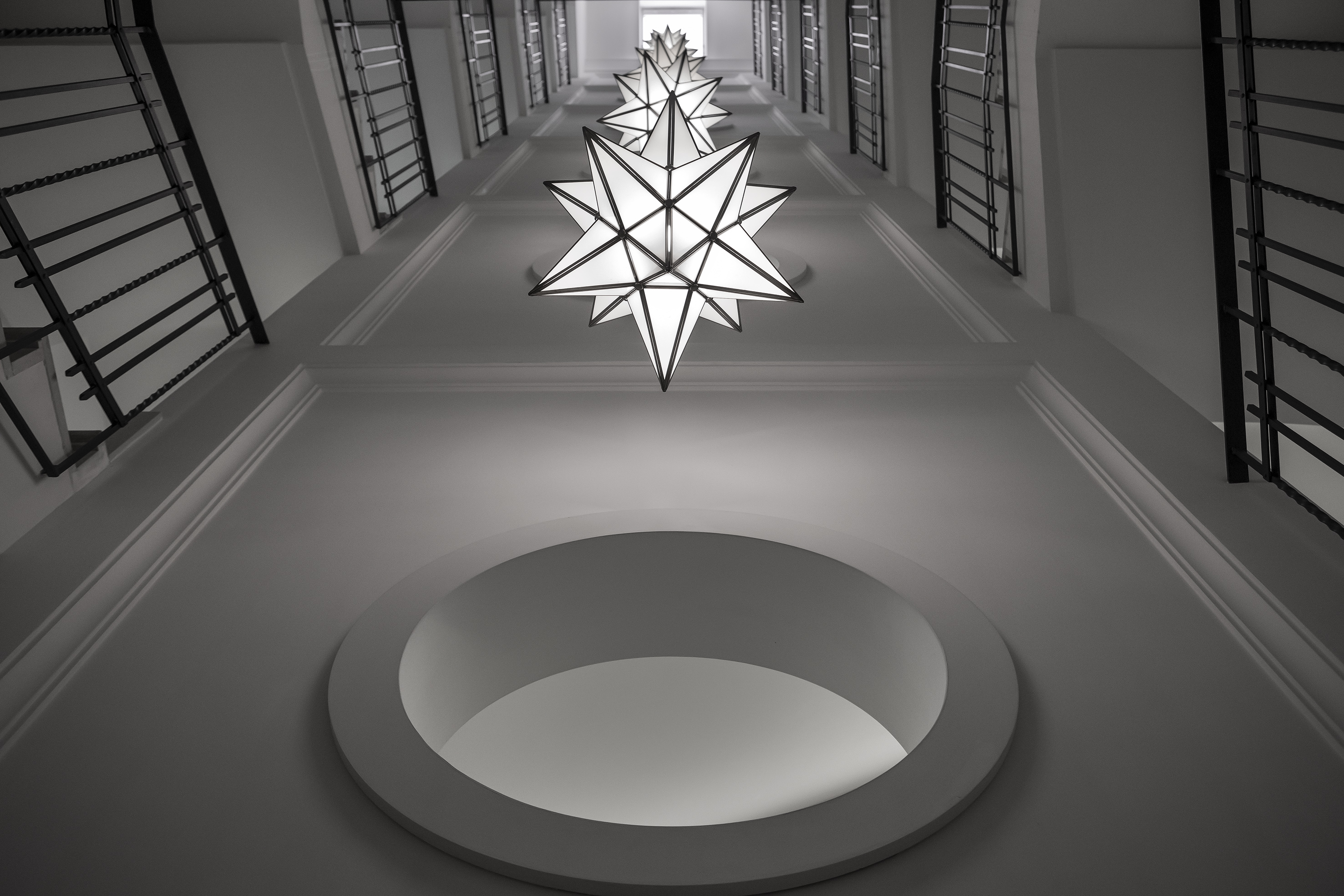 Modern white stairwell, star-shaped lights, black railings, circular ceiling.