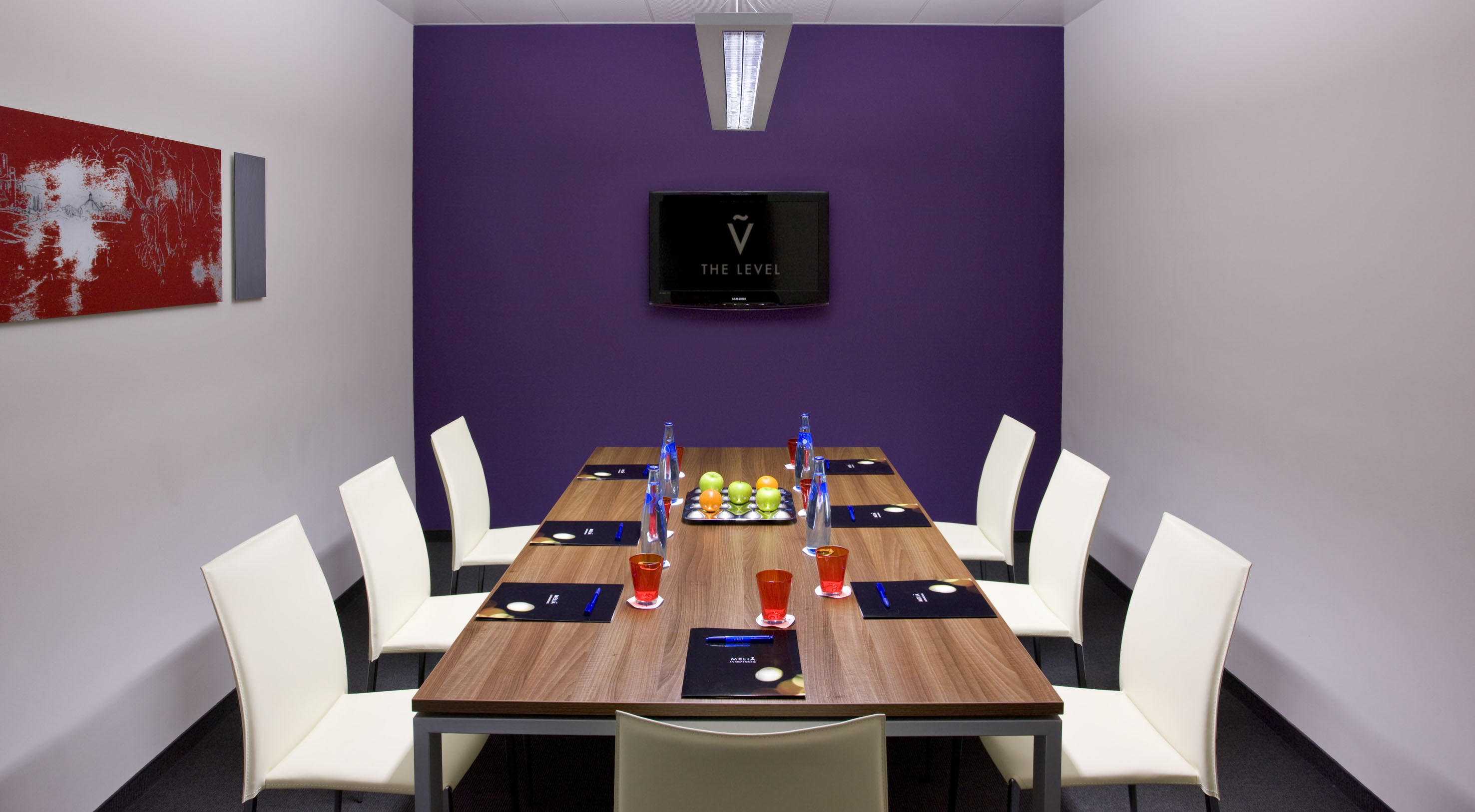 Modern conference room with purple wall, wooden table, white chairs, and TV.
