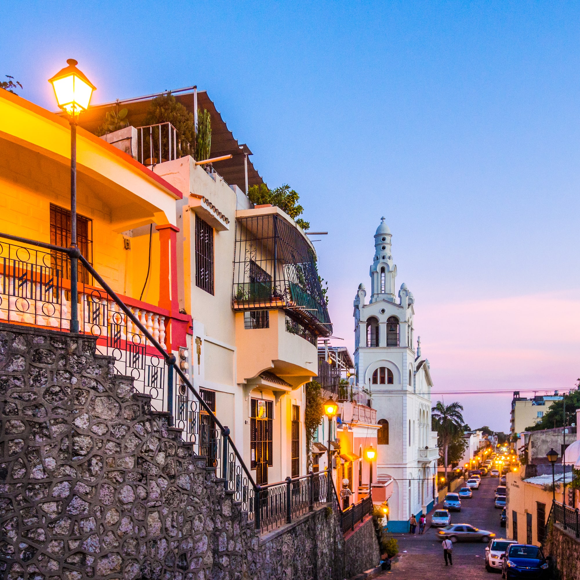 Calle colonial de Santo Domingo al anochecer, con casas coloridas e iglesia.