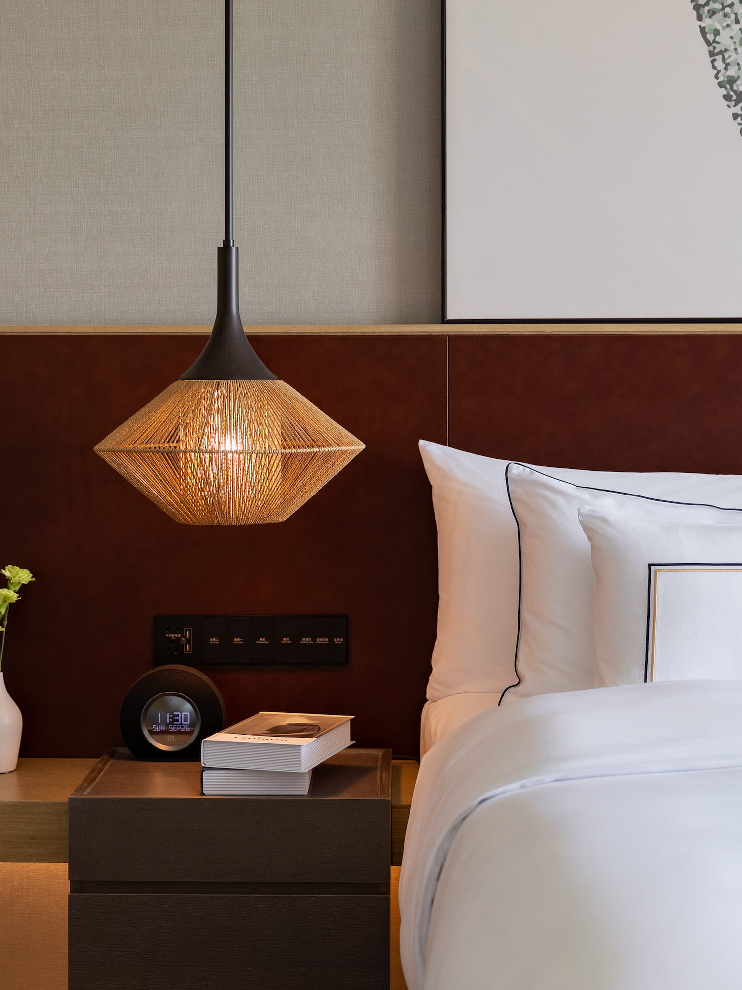 Modern hotel room with white bed, woven pendant light, and wood nightstand.