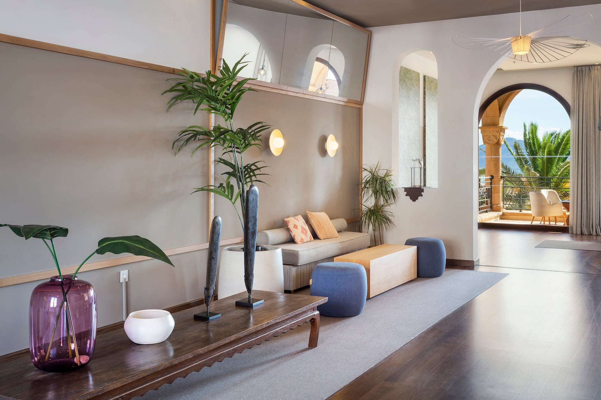 Elegant hotel lounge with sofa, tropical plants, and arched balcony mountain view.