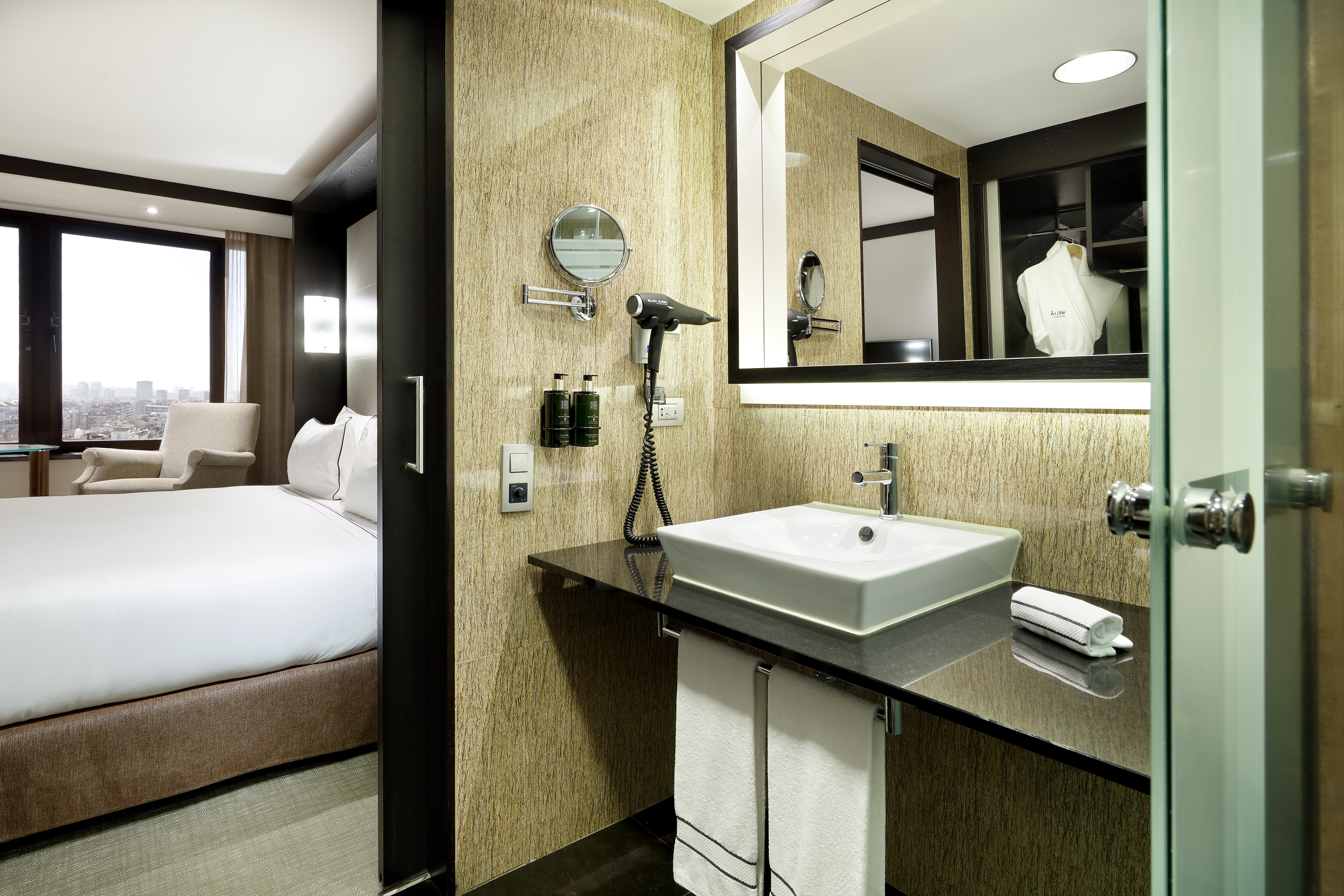 Modern hotel bathroom and bedroom interior with vanity, sink, and city view.