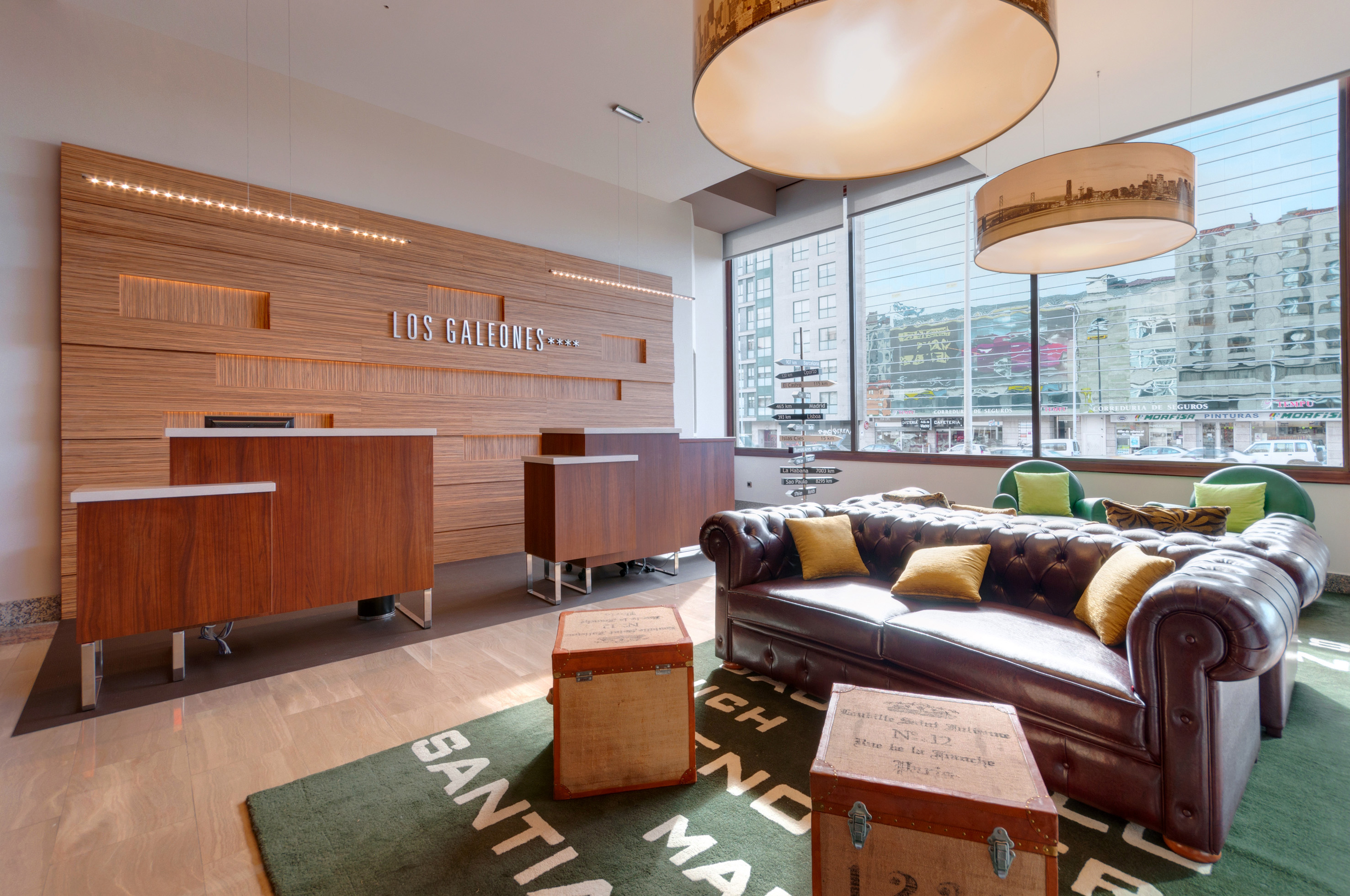Los Galeones hotel lobby with wood reception, leather sofa, and city views.