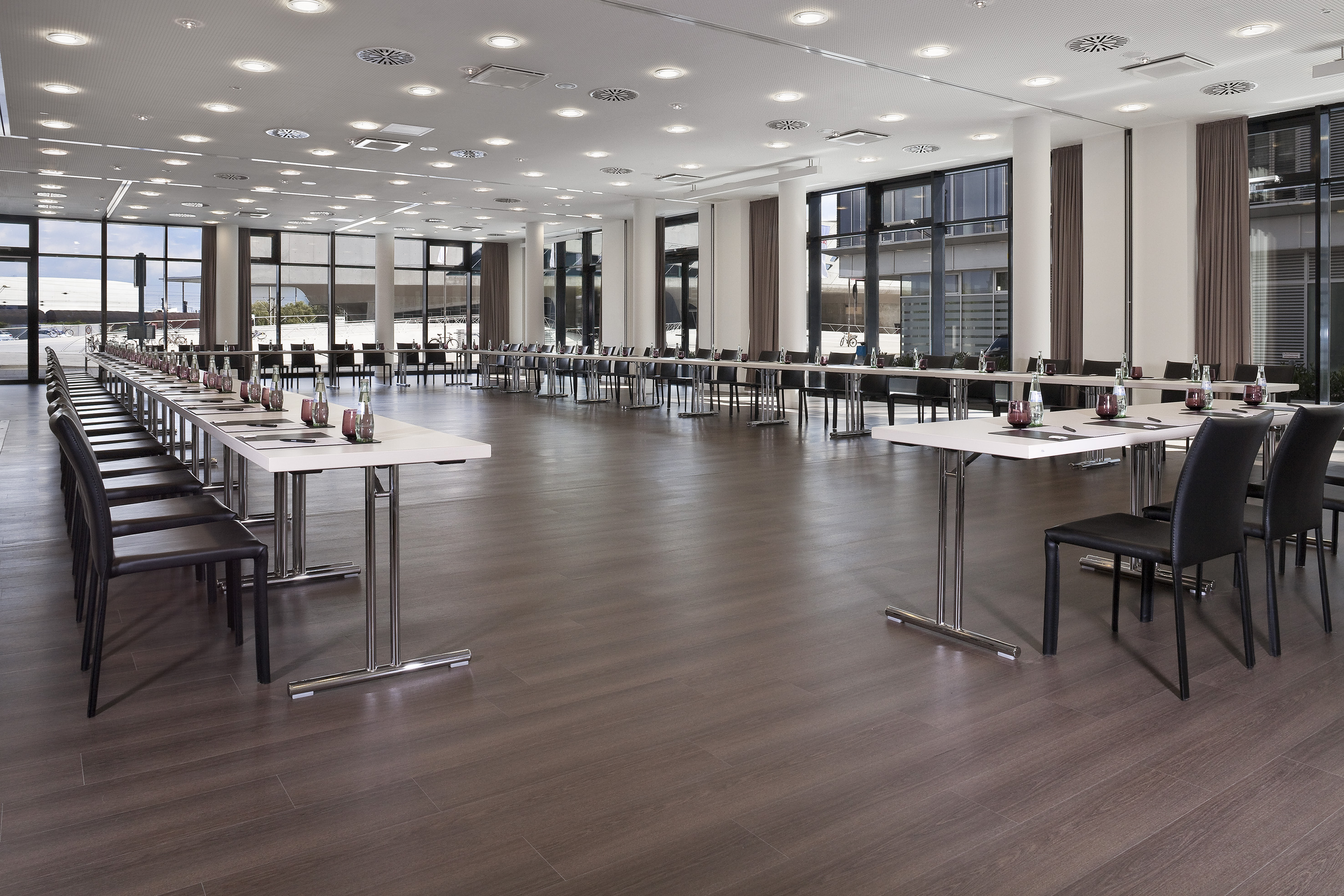 Spacious meeting room setup with tables, chairs, and large windows. - Volkswagen - INNSiDE Wolfsburg, Wolfsburg