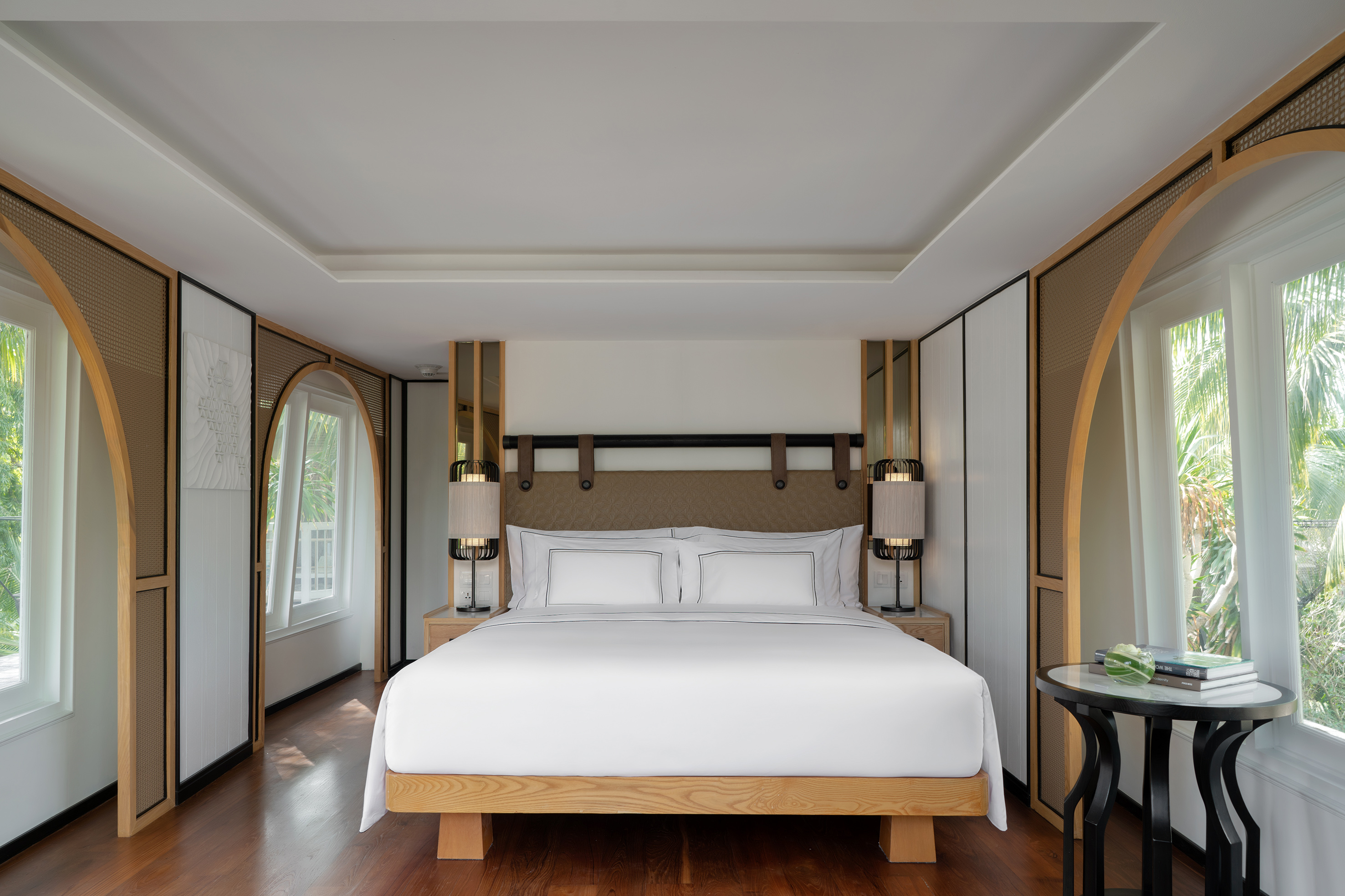 Luxury hotel bedroom with modern wood arch decor, king bed, and lush tropical views.