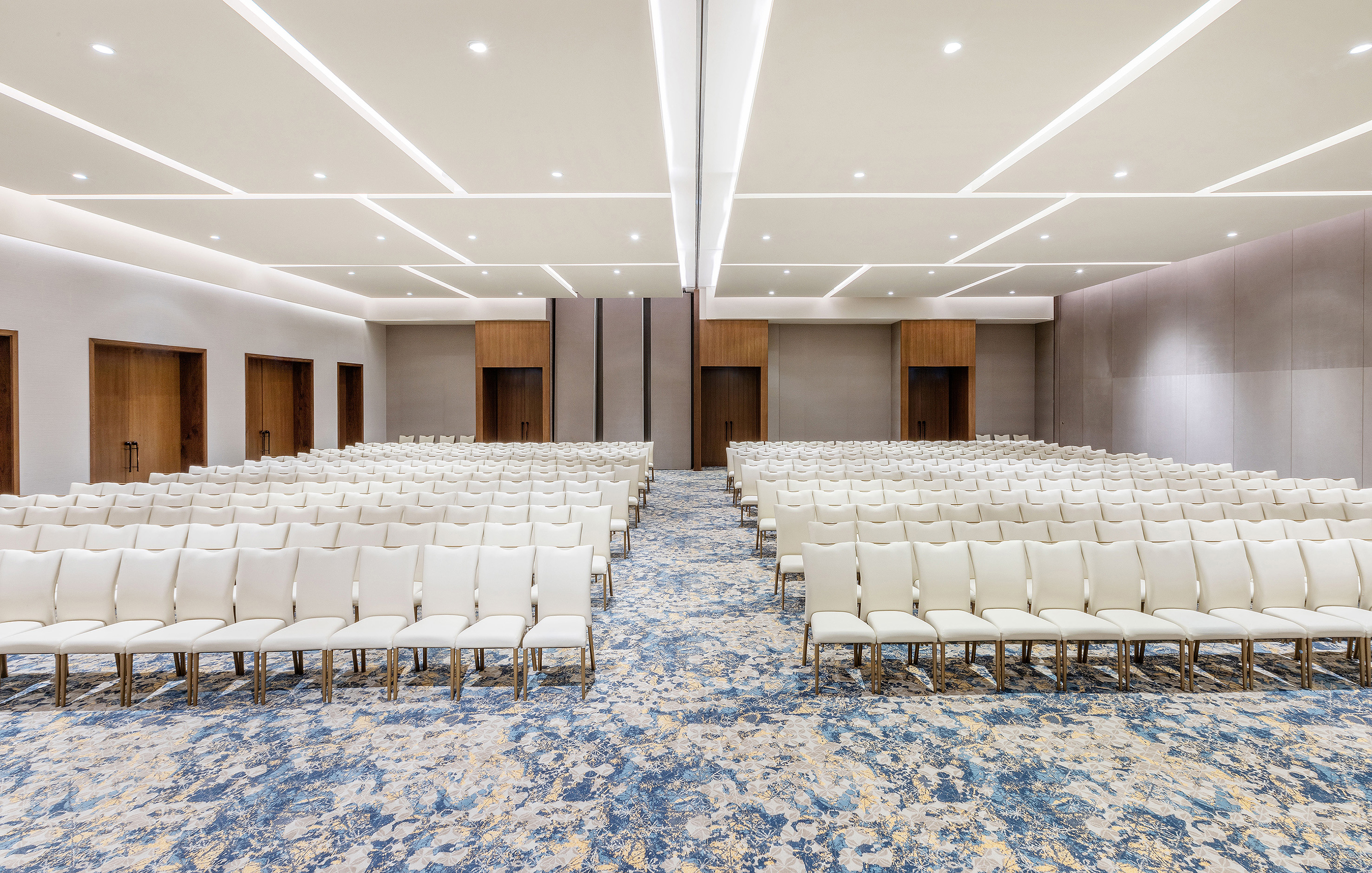 Empty ballroom with rows of white chairs, blue carpet, and modern lighting.