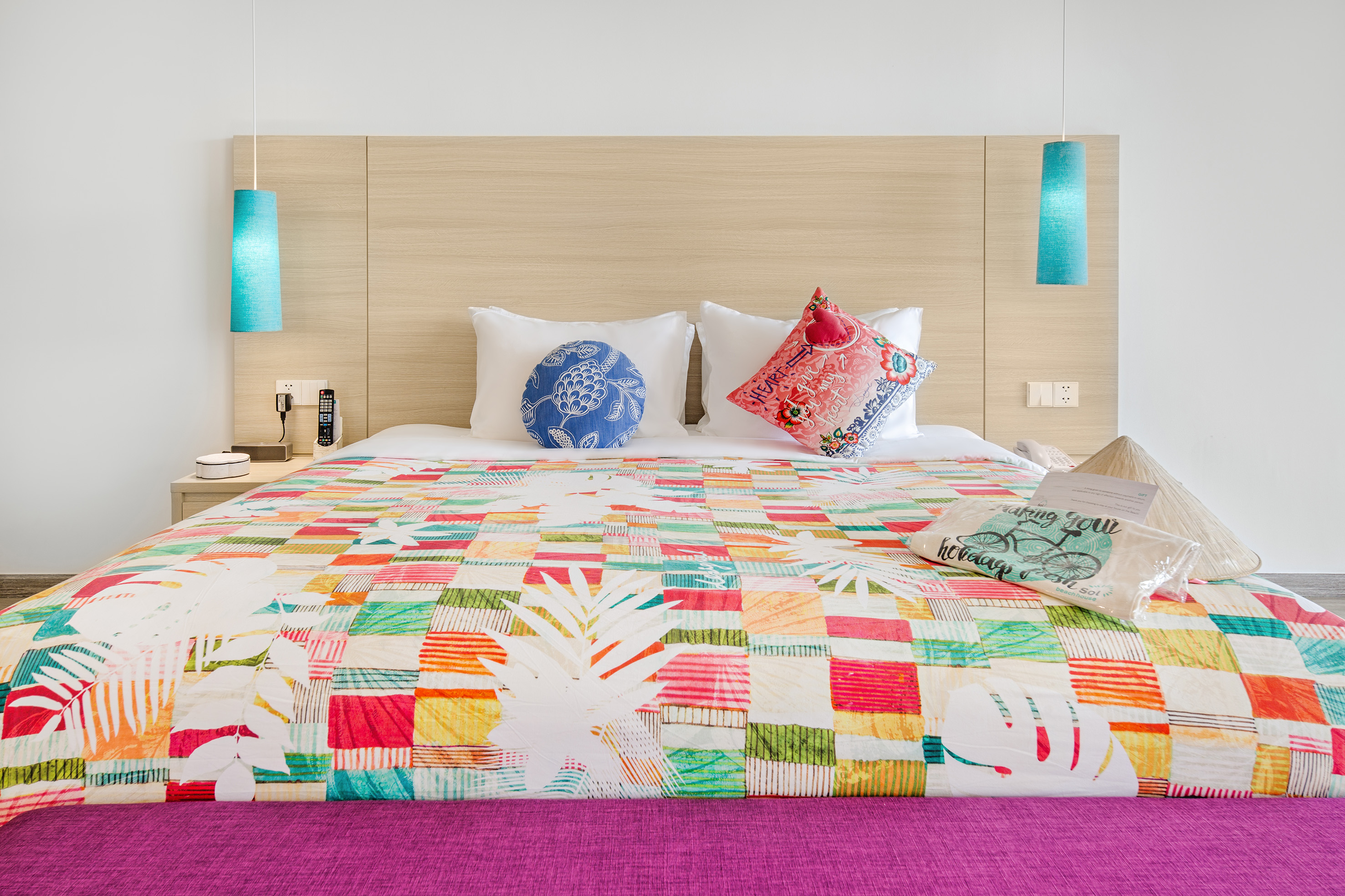 Tropical hotel bed with colorful patchwork quilt and wood headboard.