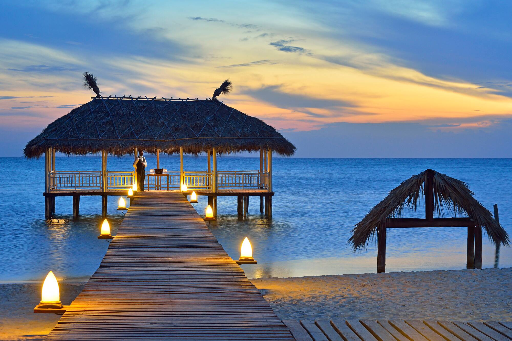 a dock with a hut and a thatched roof on the water