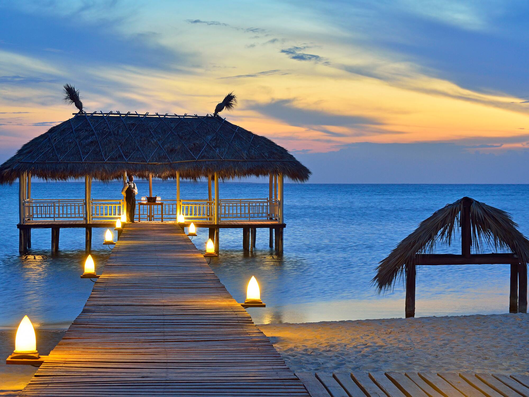 a dock with a hut and a thatched roof on the water