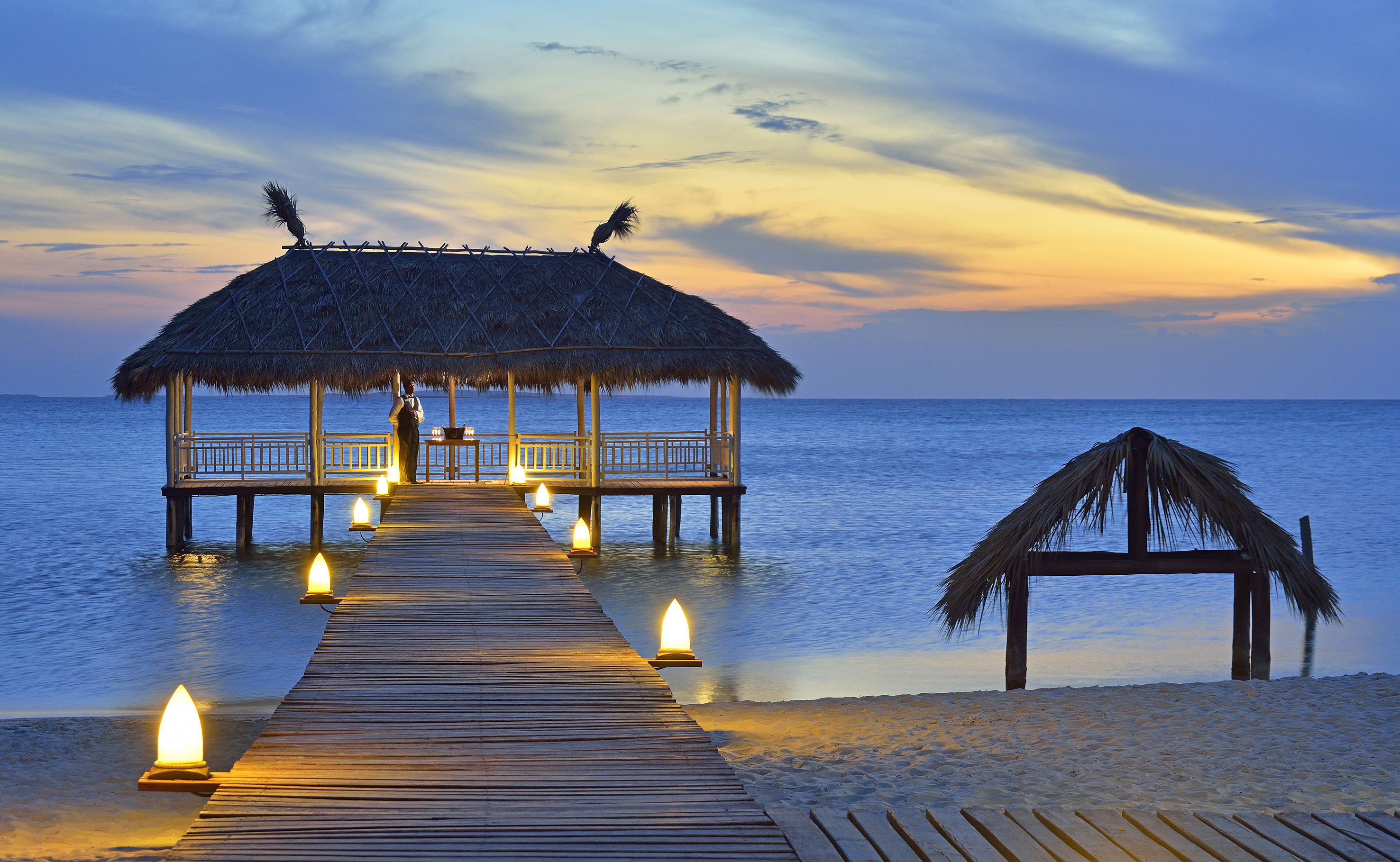 a dock with a hut and a thatched roof on the water