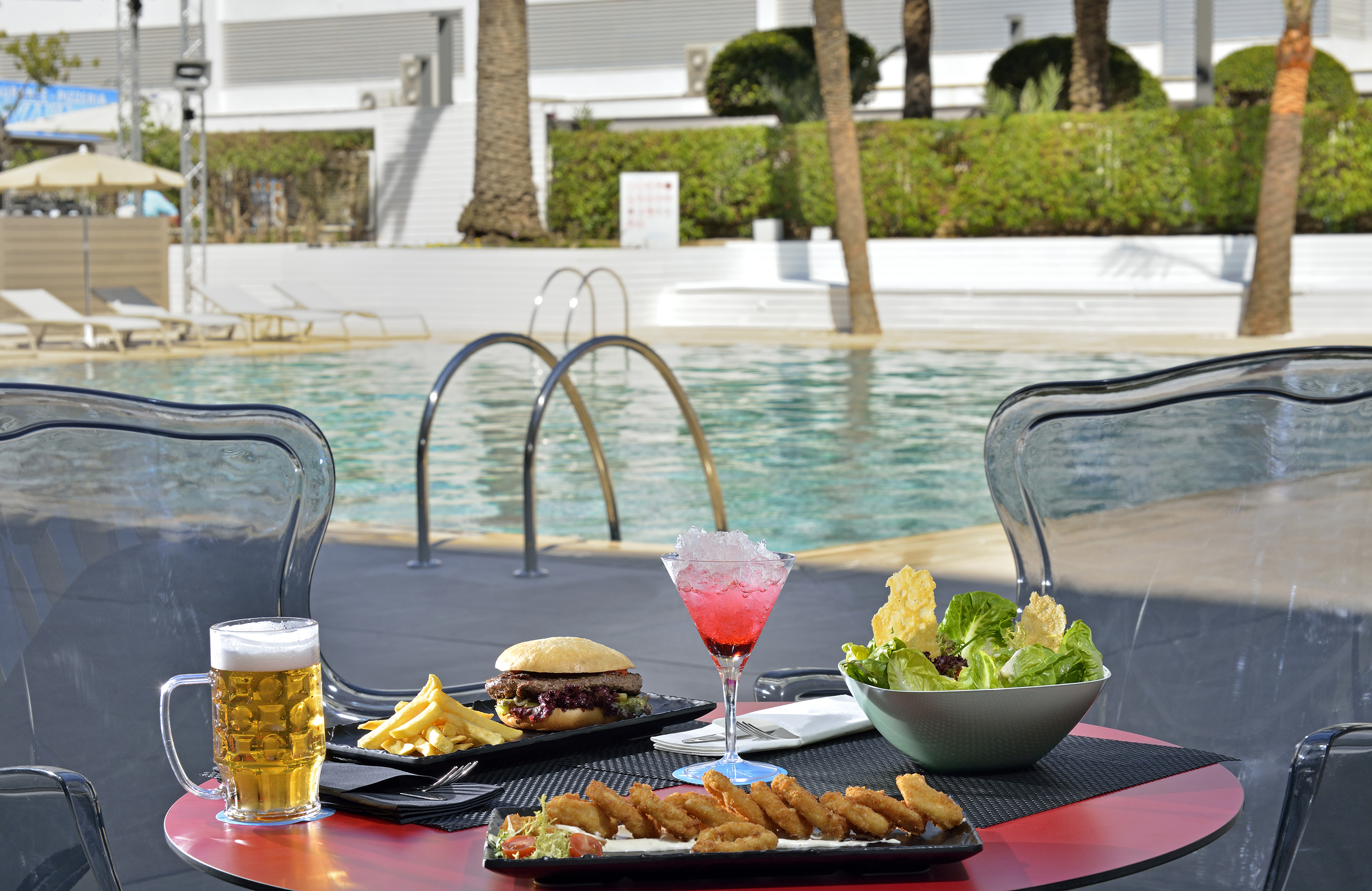 Poolside dining: burger, fries, salad, fried seafood, red cocktail, and beer.