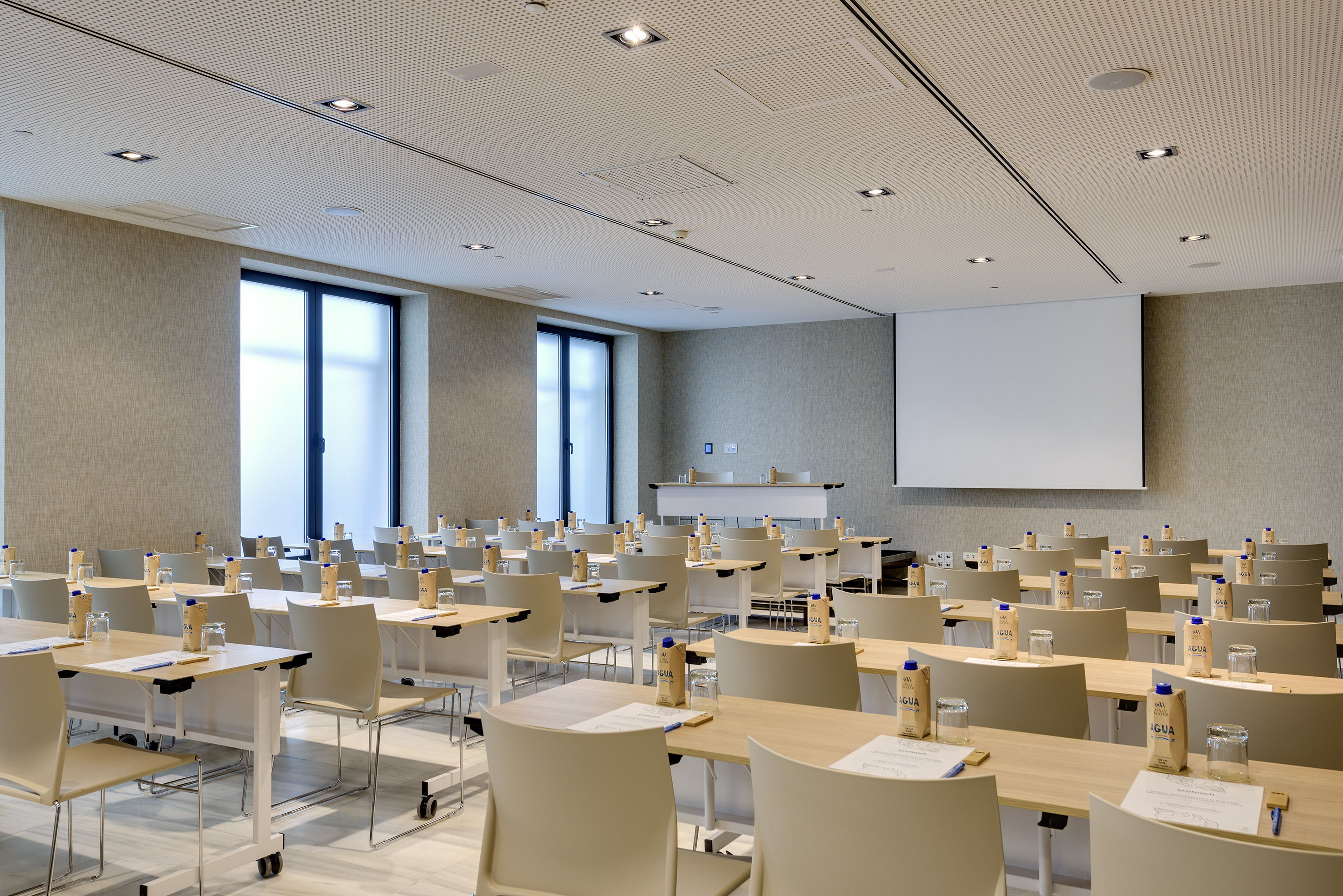 Empty modern conference room, classroom setup, projector screen, large windows.