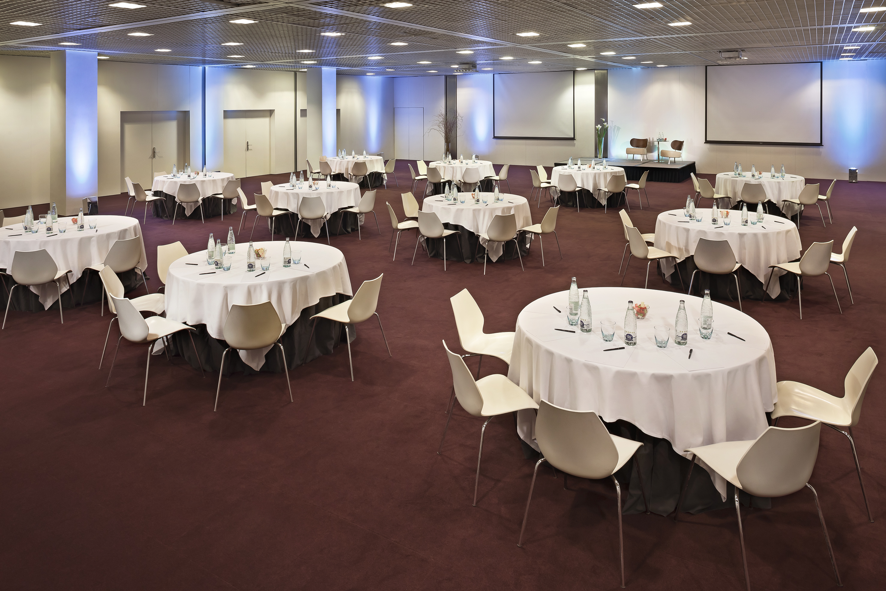 Event space with round tables, white chairs, and projector screens for conferences.
