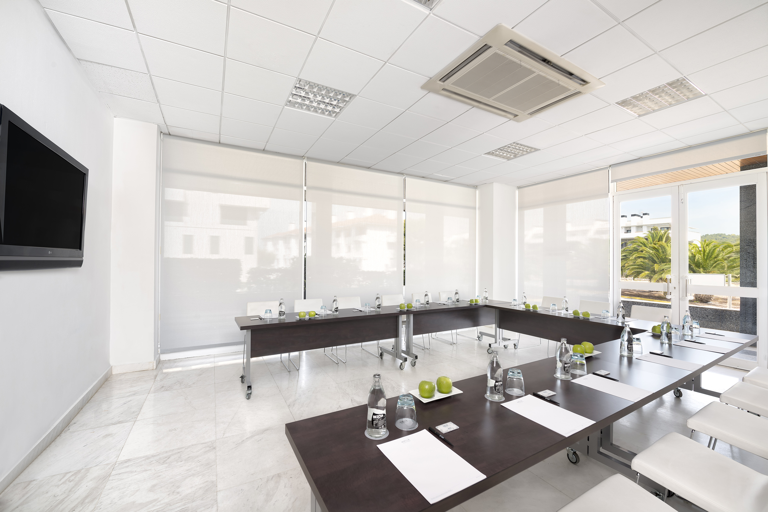 Modern conference room with U-shaped table, TV screen, and bright outdoor view.