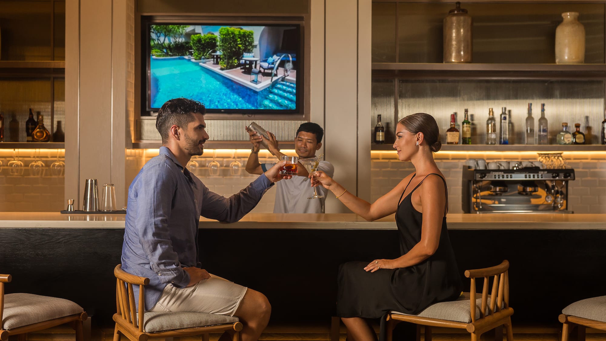 a man and woman sitting at a bar toasting with drinks