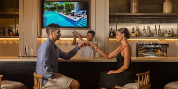 a man and woman sitting at a bar toasting with drinks