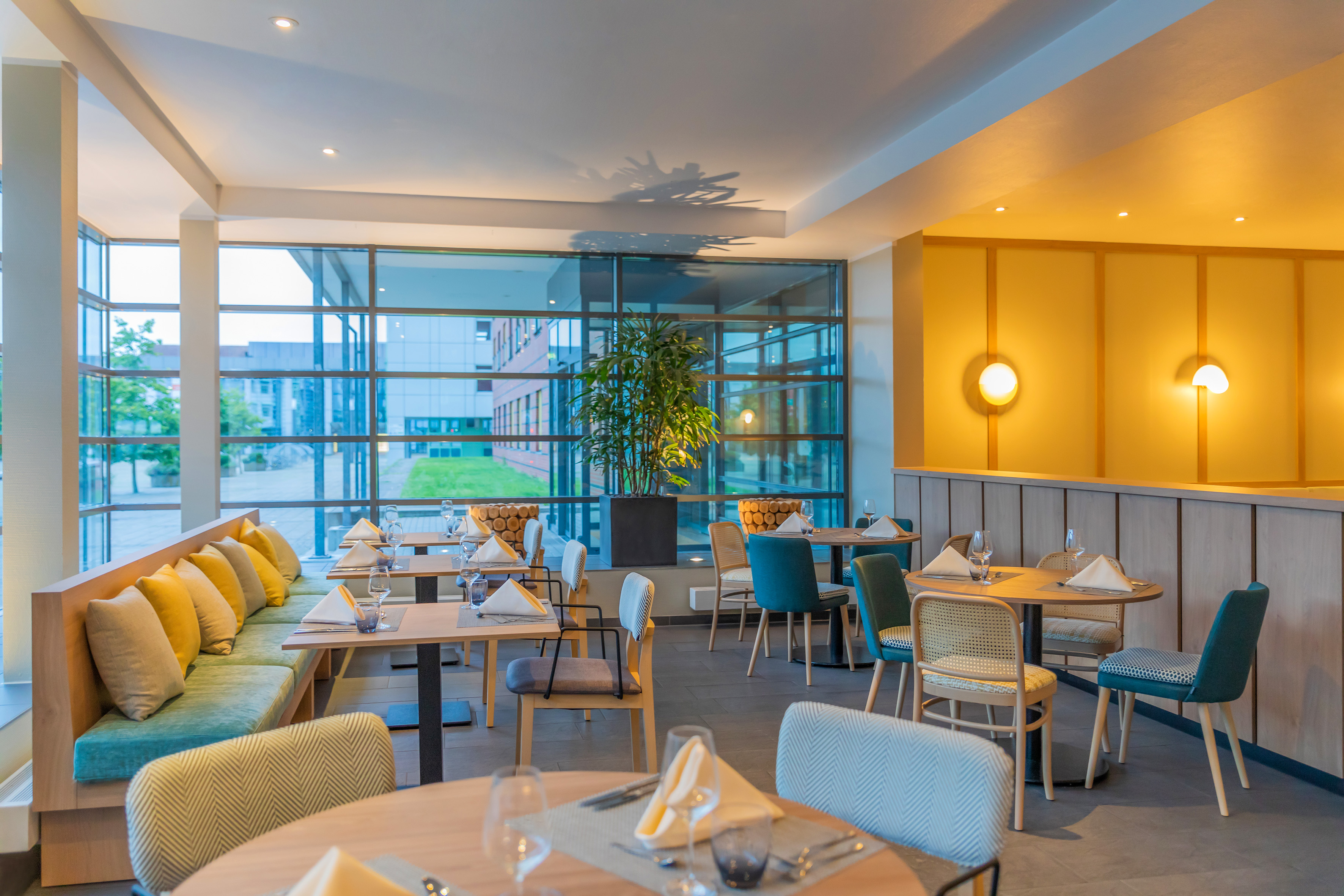 Modern restaurant dining room with set tables, banquette seating, and large windows.