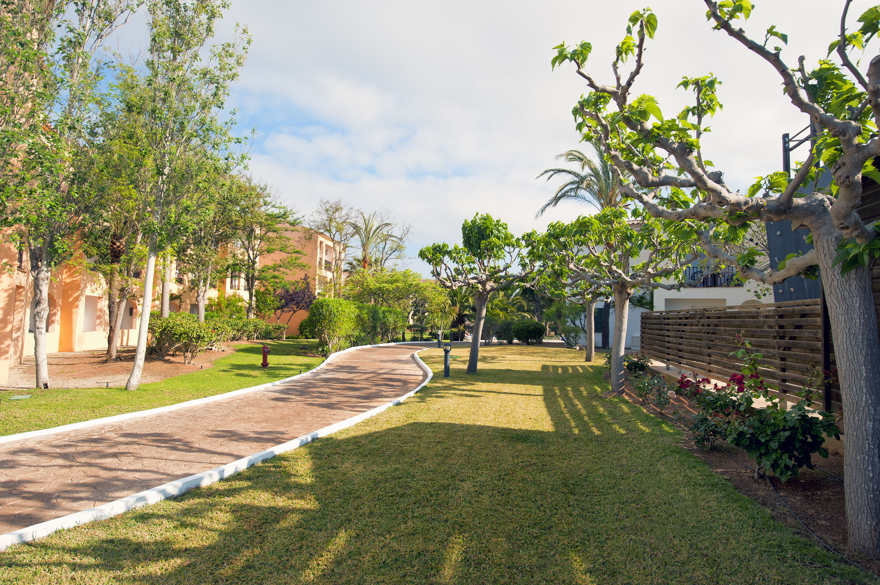 Resort garden pathway with lush green grass, trees, and hotel buildings.