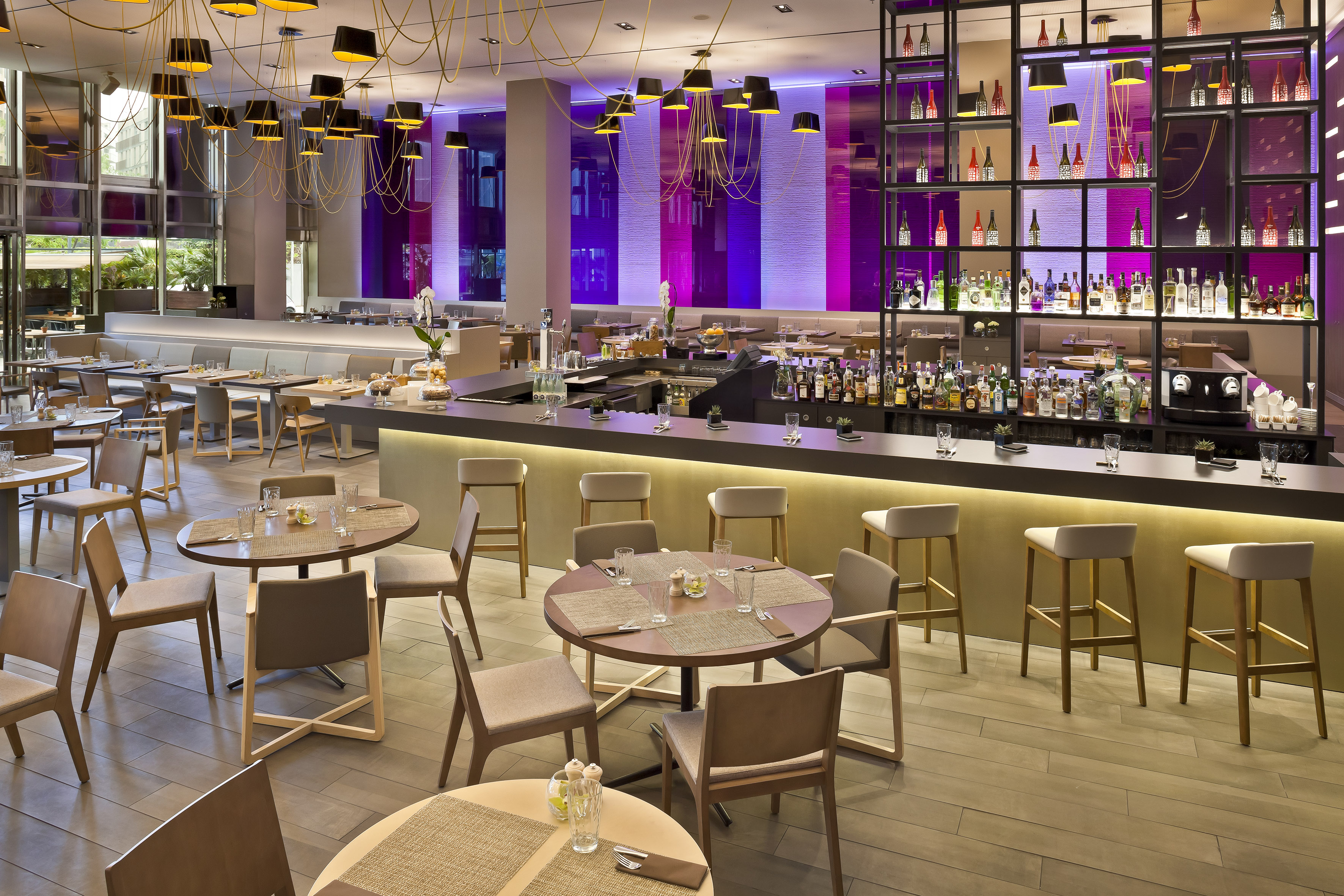 Modern hotel bar and restaurant with dining tables, bar stools, purple lighting.