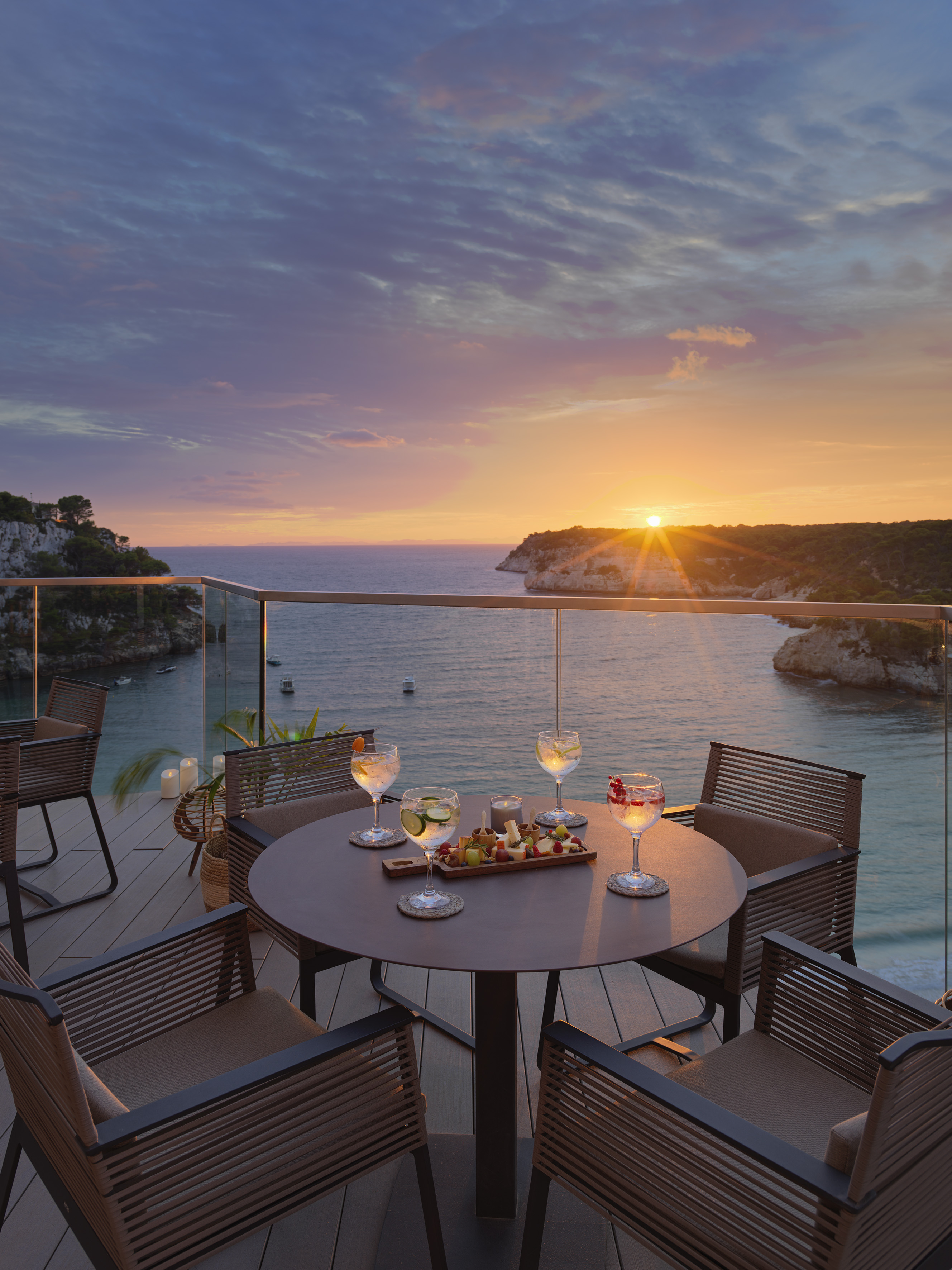 Luxury balcony at sunset over ocean, with cocktails and appetizers.
