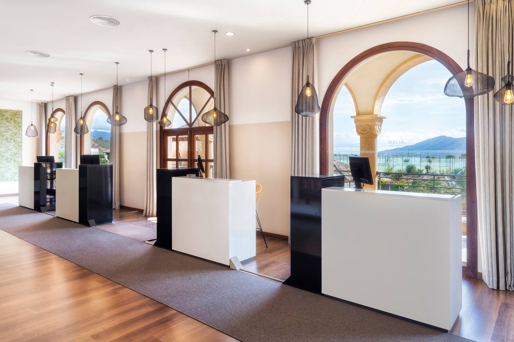 Meliá hotel reception with sleek white desks, arched windows, and mountain view.