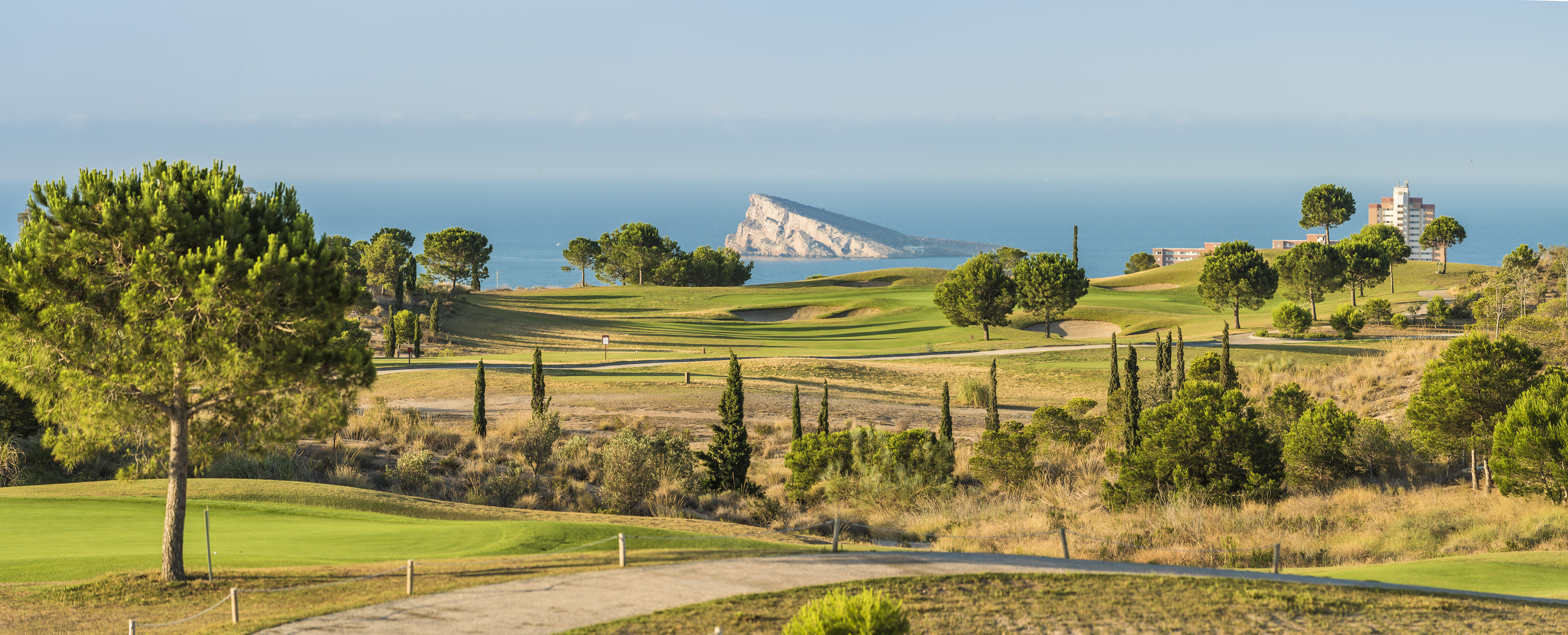 Coastal golf course with sea view, rocky island, green fairways, and pine trees.