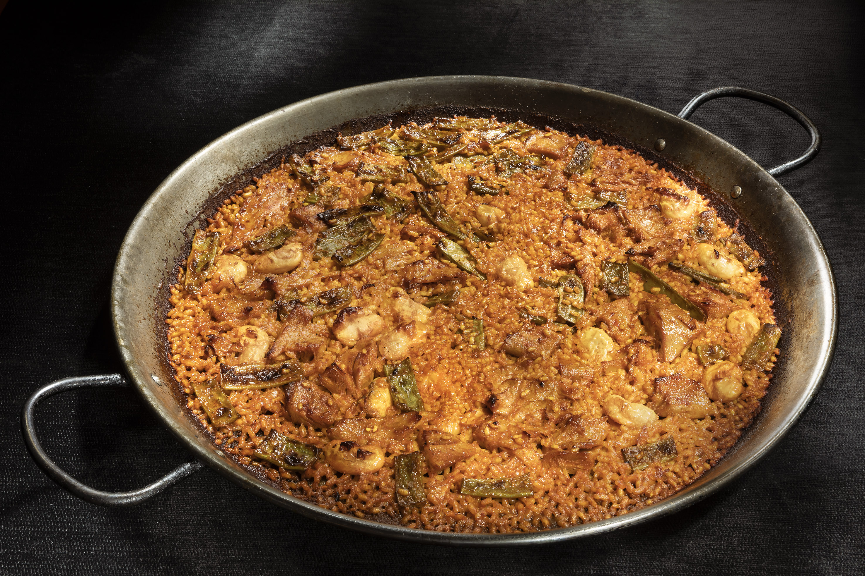 Valencian paella with chicken, snails, and green beans in a large pan.