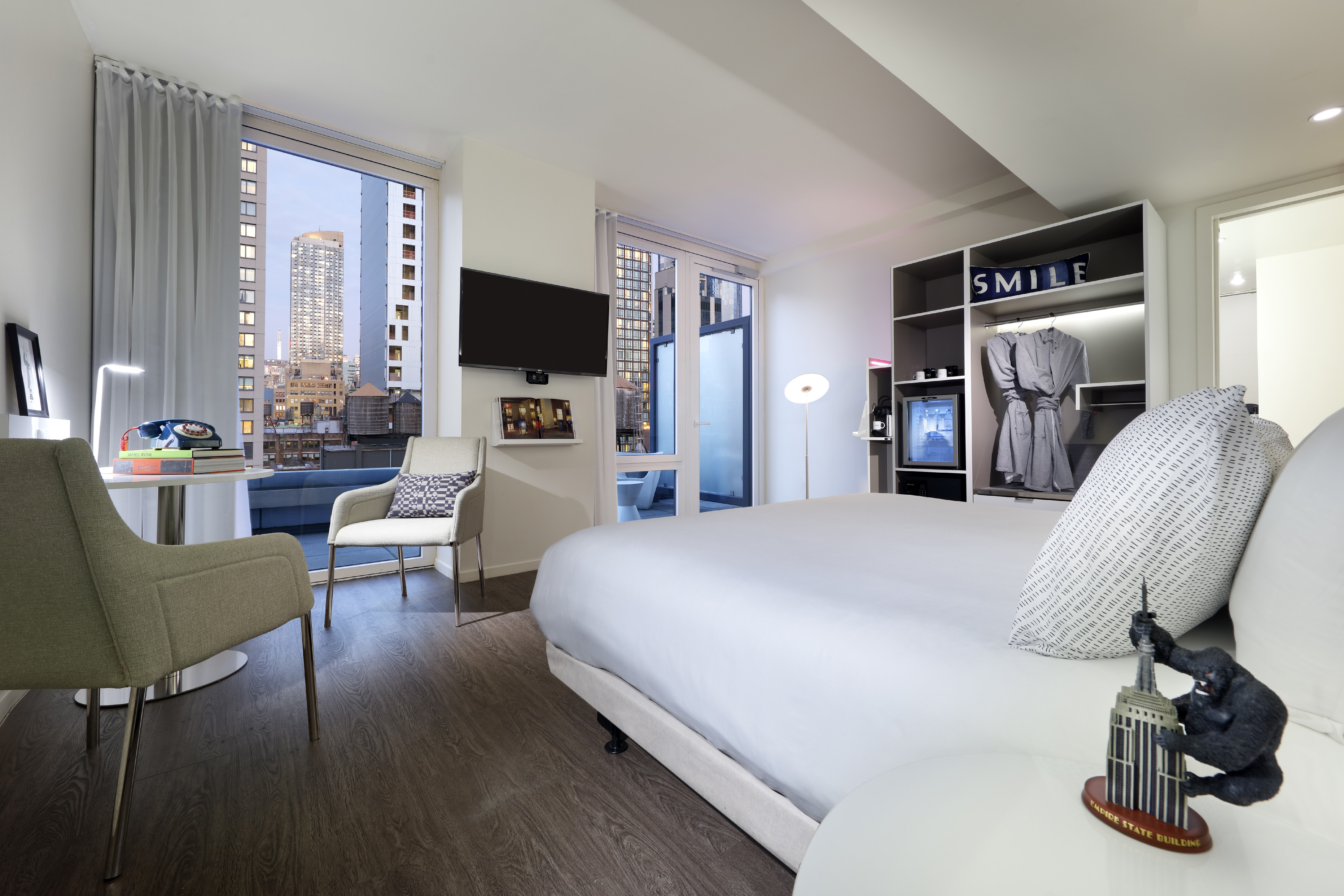 Modern hotel room overlooking NYC skyline, with large bed and work area.