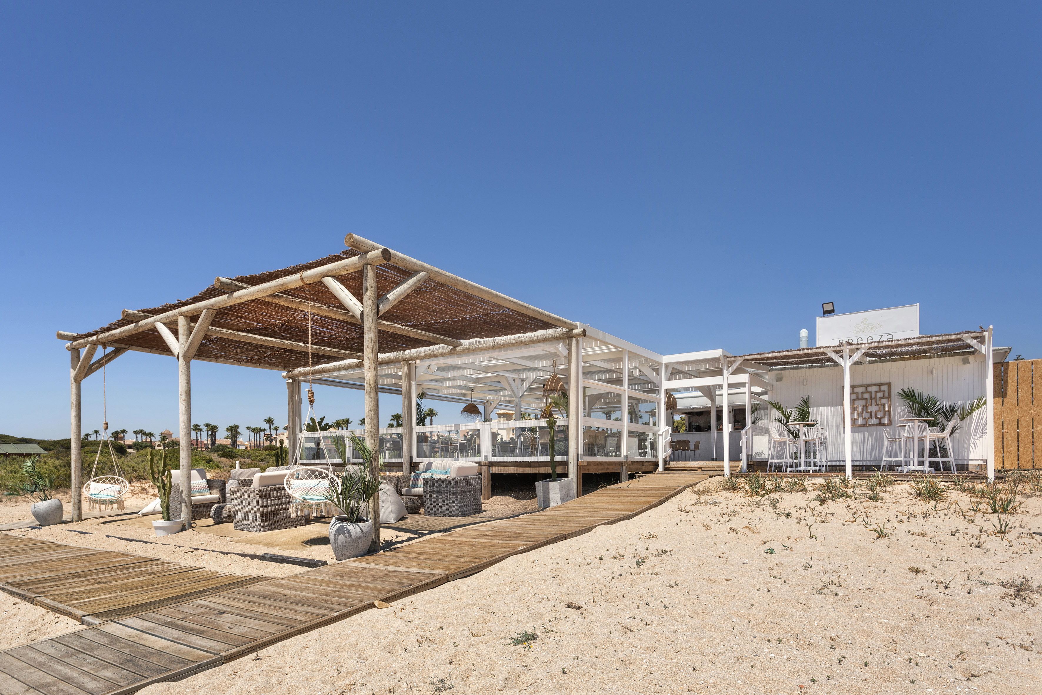 Breeza beach restaurant with outdoor lounge and wooden boardwalk on sand.
