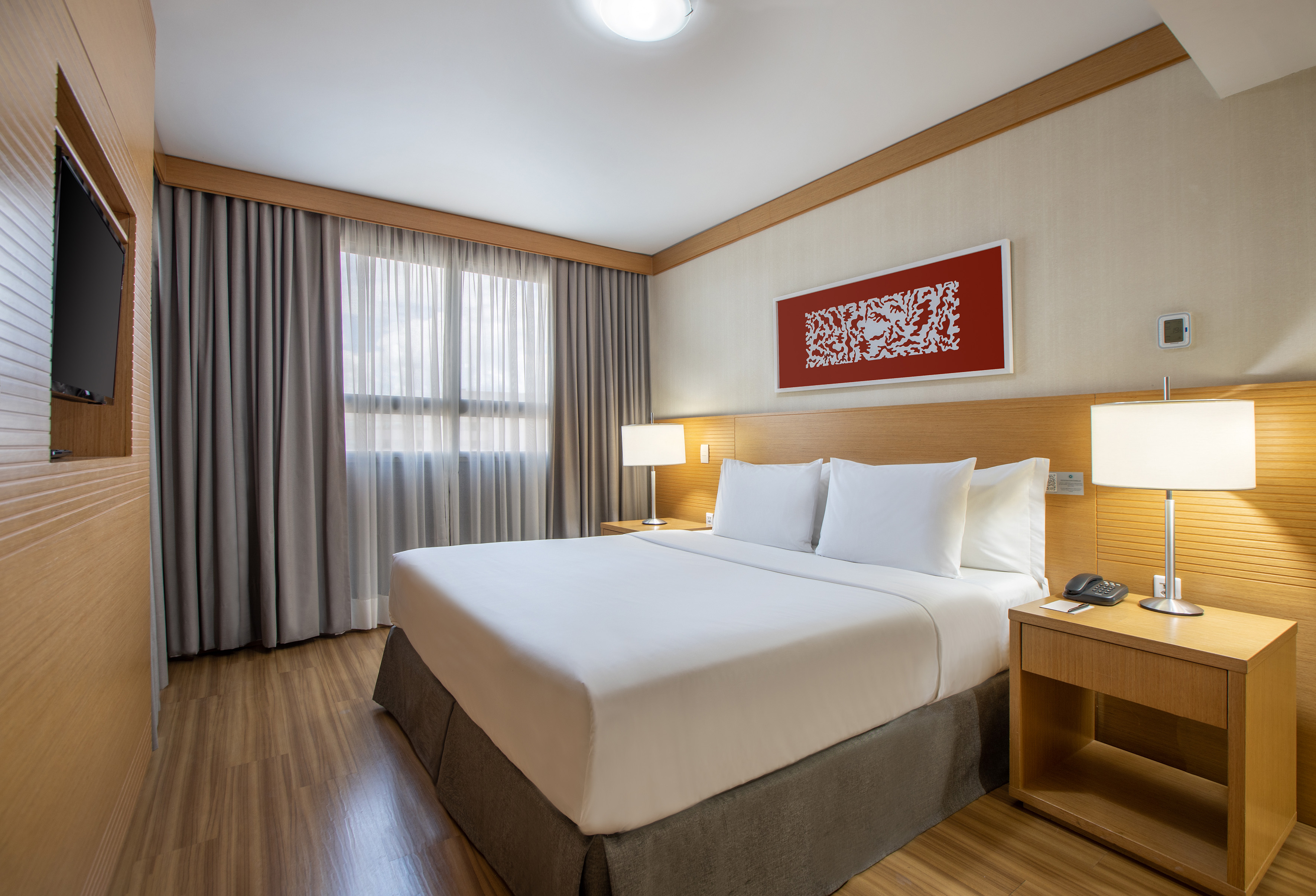 Modern hotel bedroom with large bed, wooden headboard, nightstands, and window.