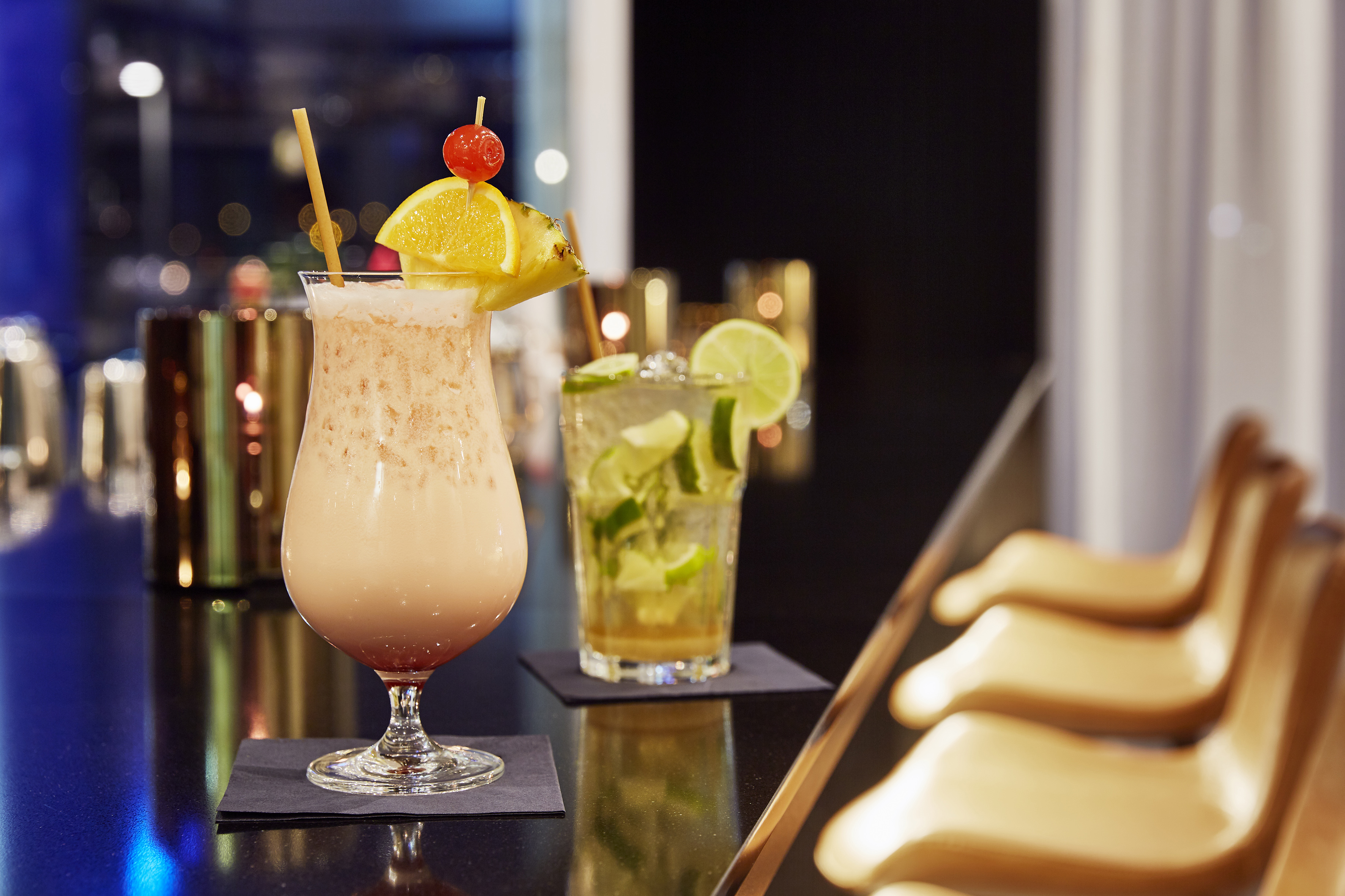 Two cocktails on a dark bar: tropical drink with fruit, lime drink.