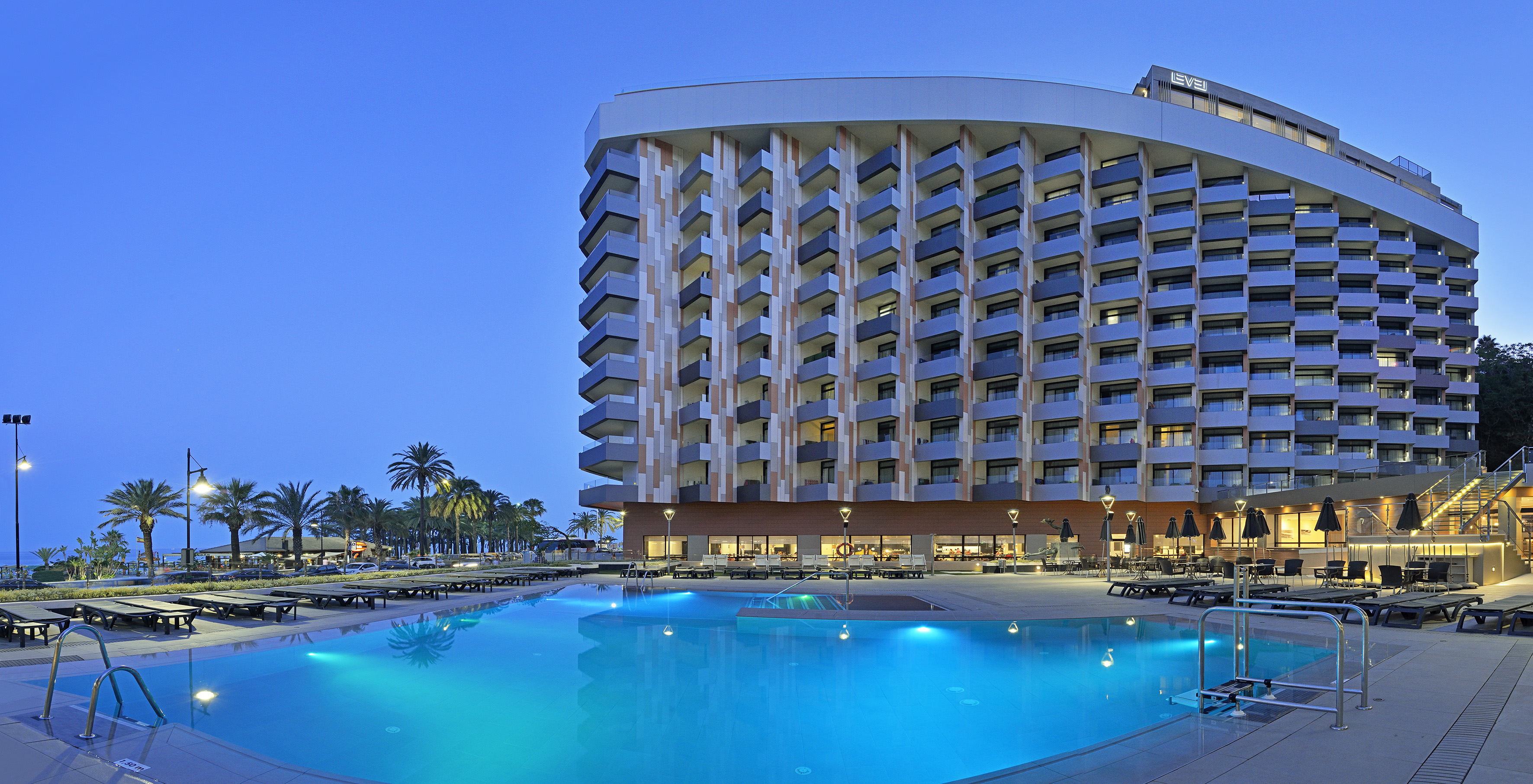 Modern resort hotel with illuminated pool and palm trees at evening.