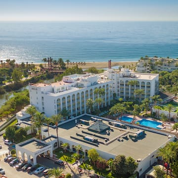 a large white building with trees and a pool by the ocean