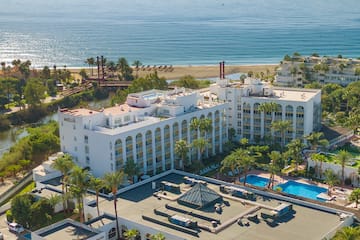a large white building with trees and a pool by the ocean
