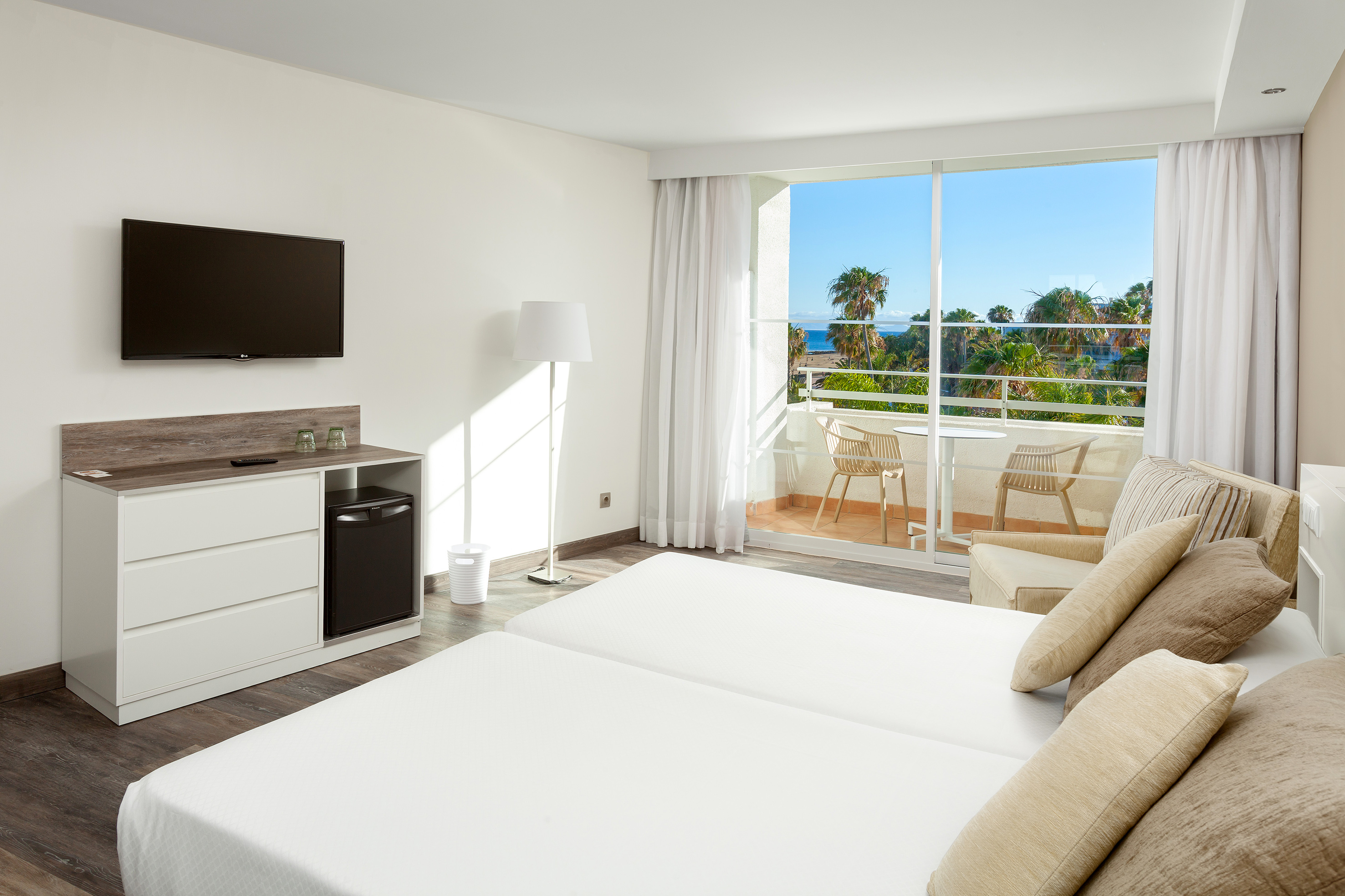 Hotel room with two beds, private balcony, sea view, and palm trees.