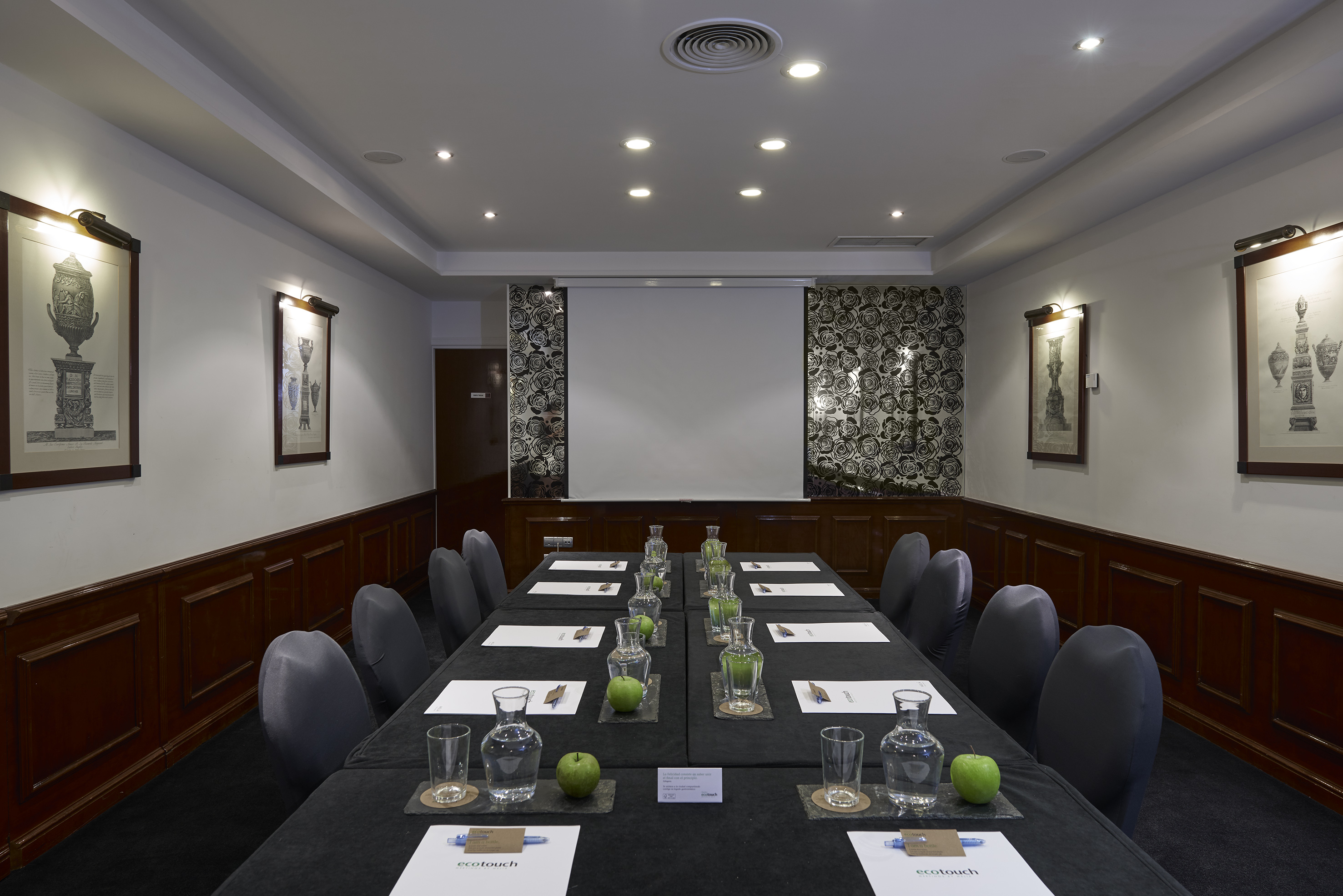Meeting room with black table, chairs, projection screen, and refreshments.