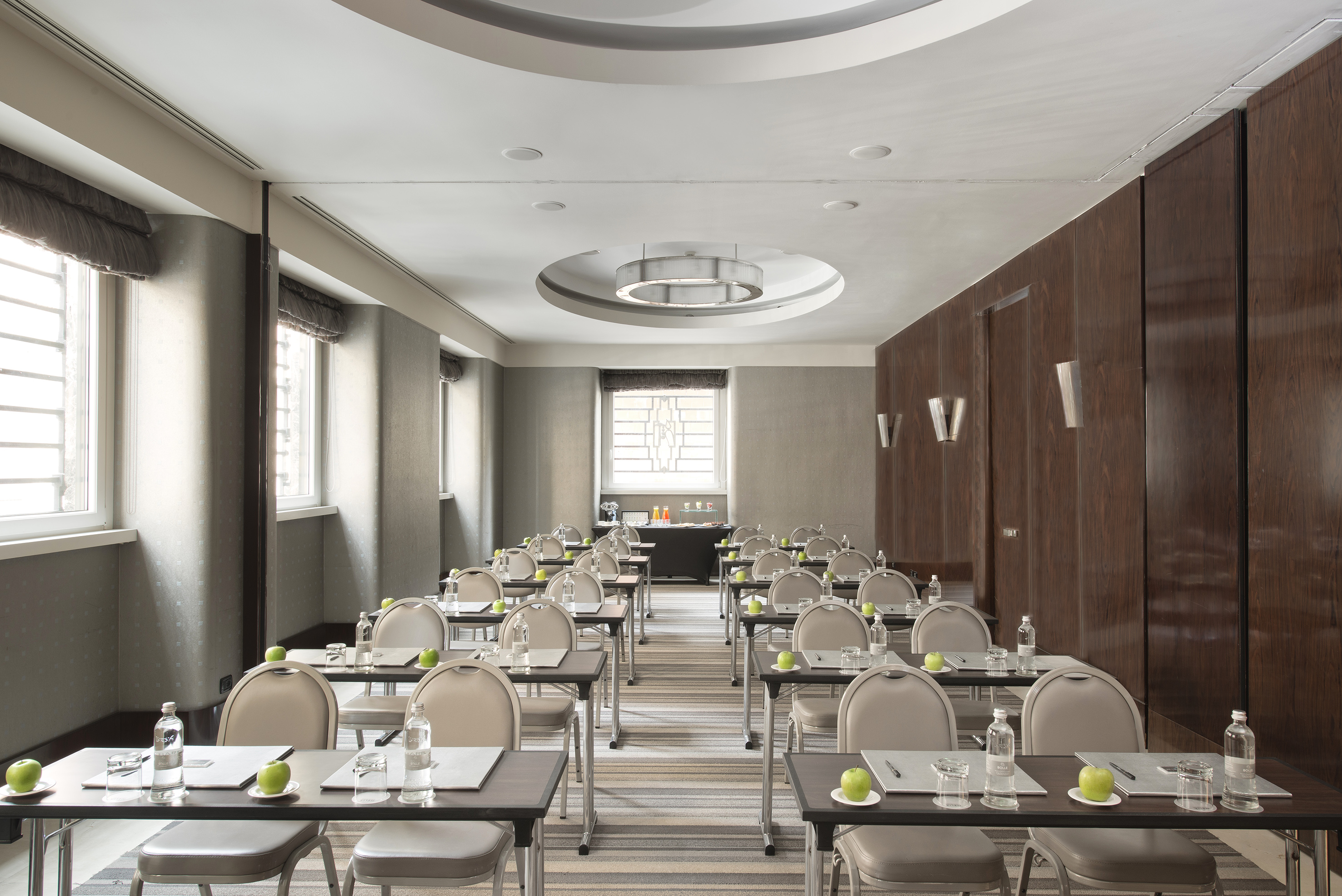 Modern conference room with rows of tables, chairs, water, and apples.