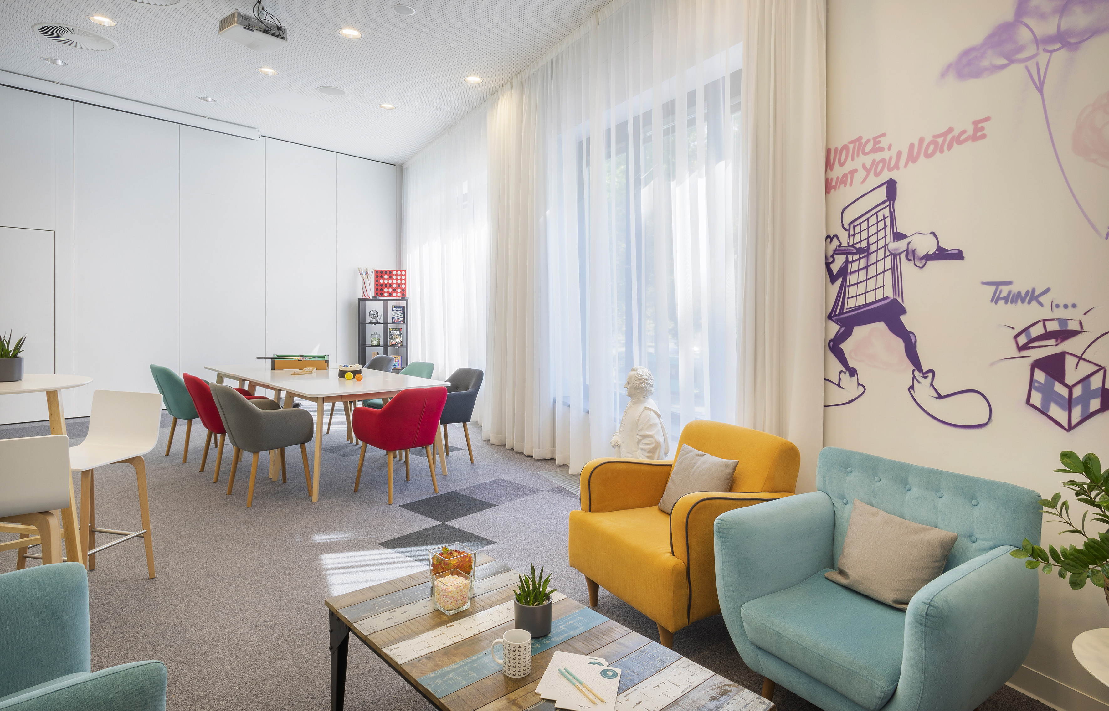 Colorful office lounge with meeting table, diverse chairs, and creative wall art.