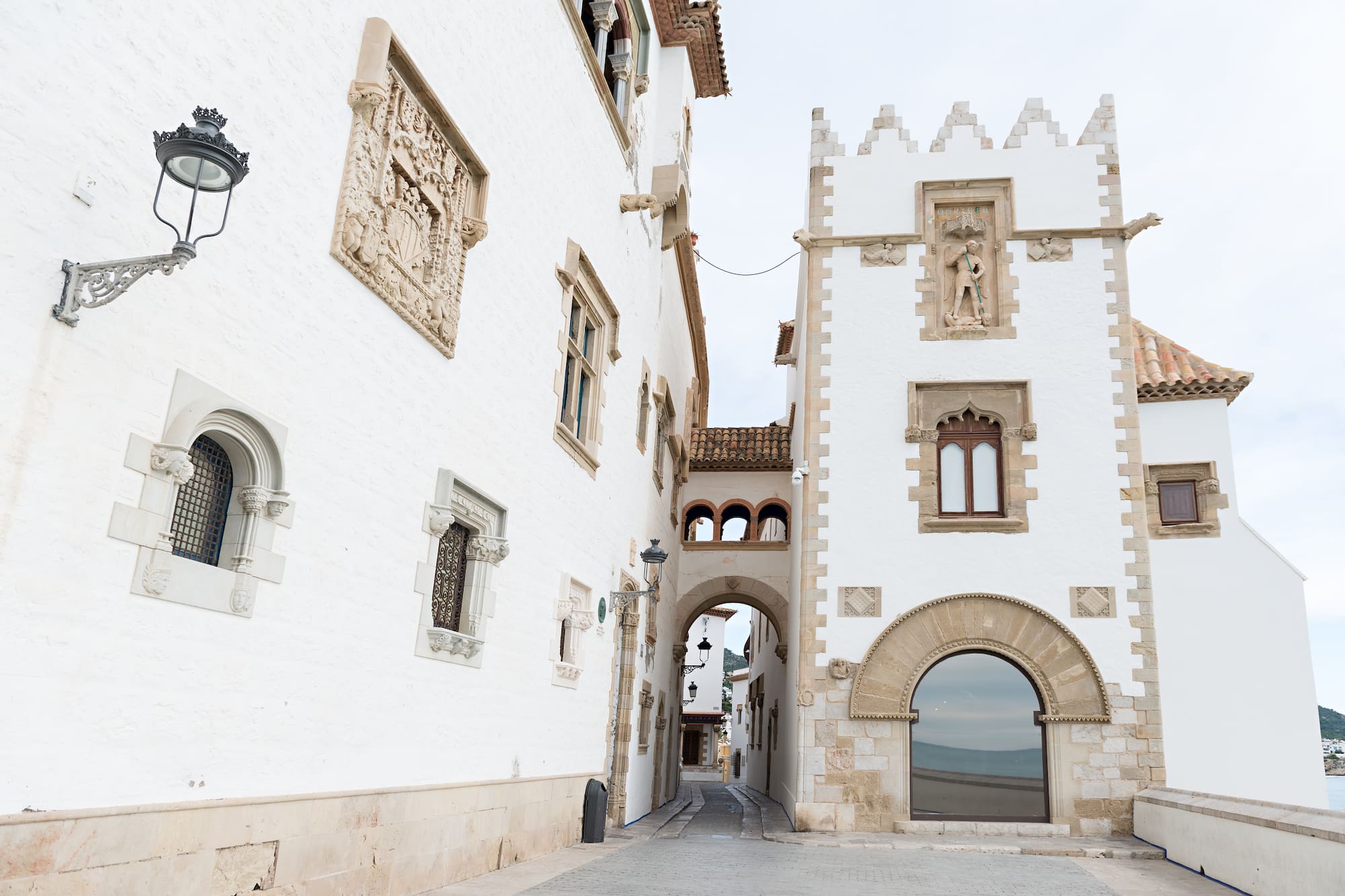 Callejón histórico en Sitges: edificios blancos, arcos y ventanas ornamentadas.